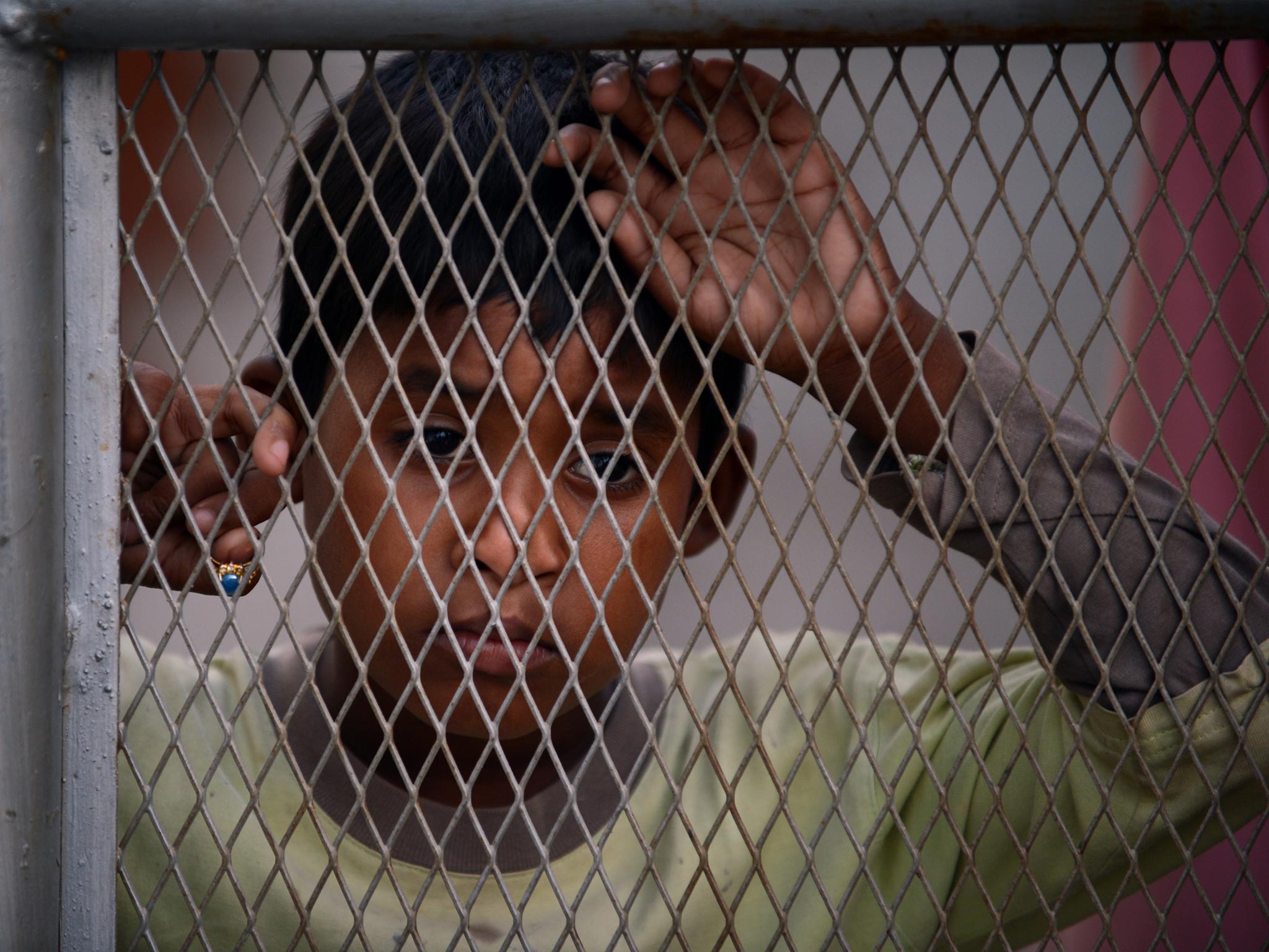 A young Myanmar Muslim Rohingya refugee looks on behind a wired fence