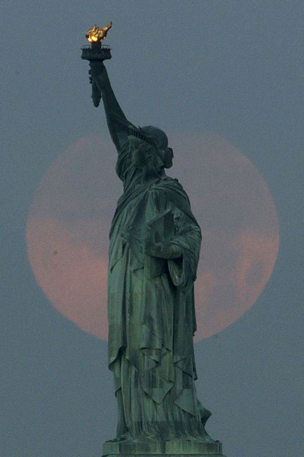 A supermoon sets behind the Statue of Liberty