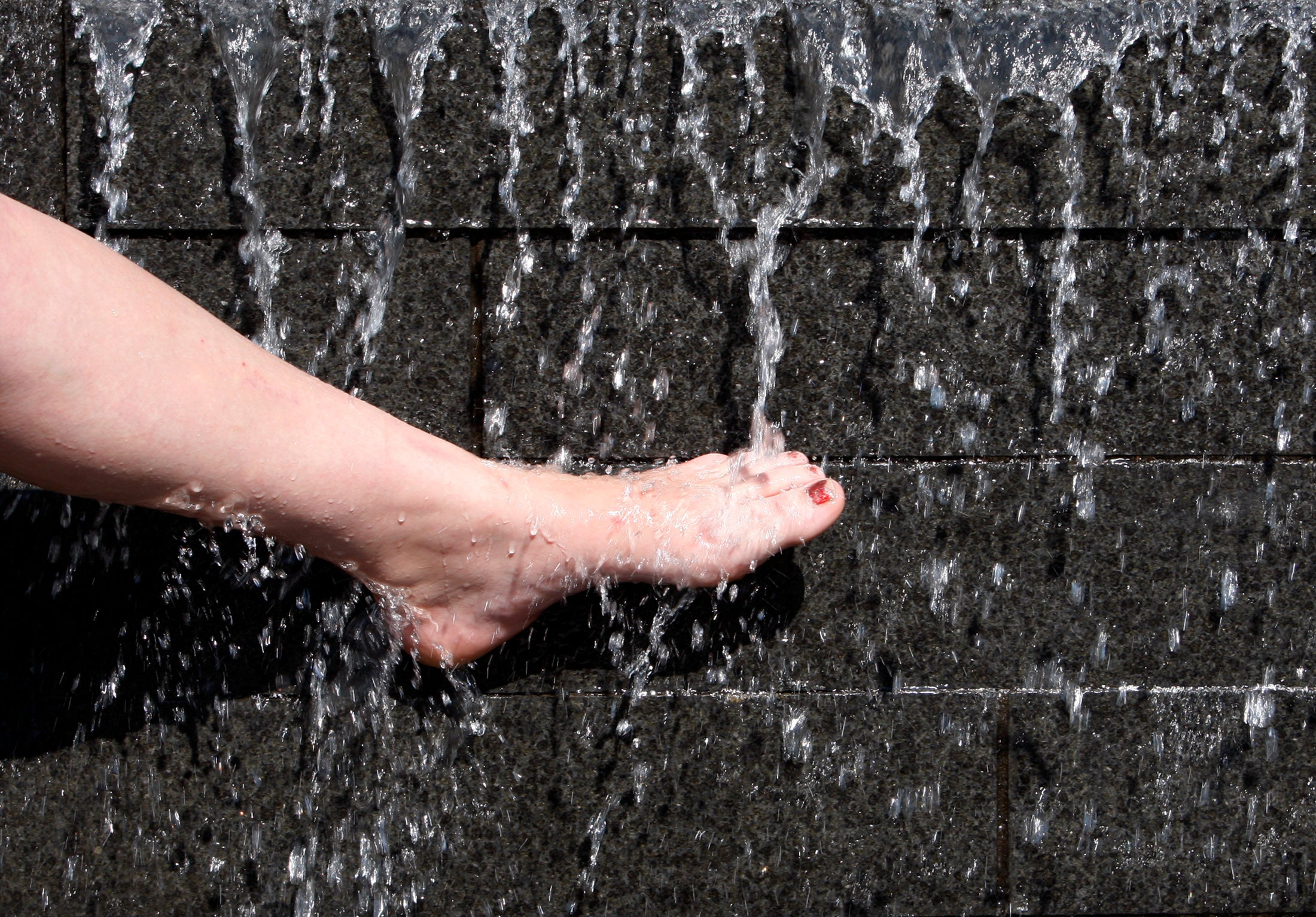 A woman cools her foot in a fountain during hot weather in Nottingham, central England May 8, 2008. REUTERS/Darren Staples