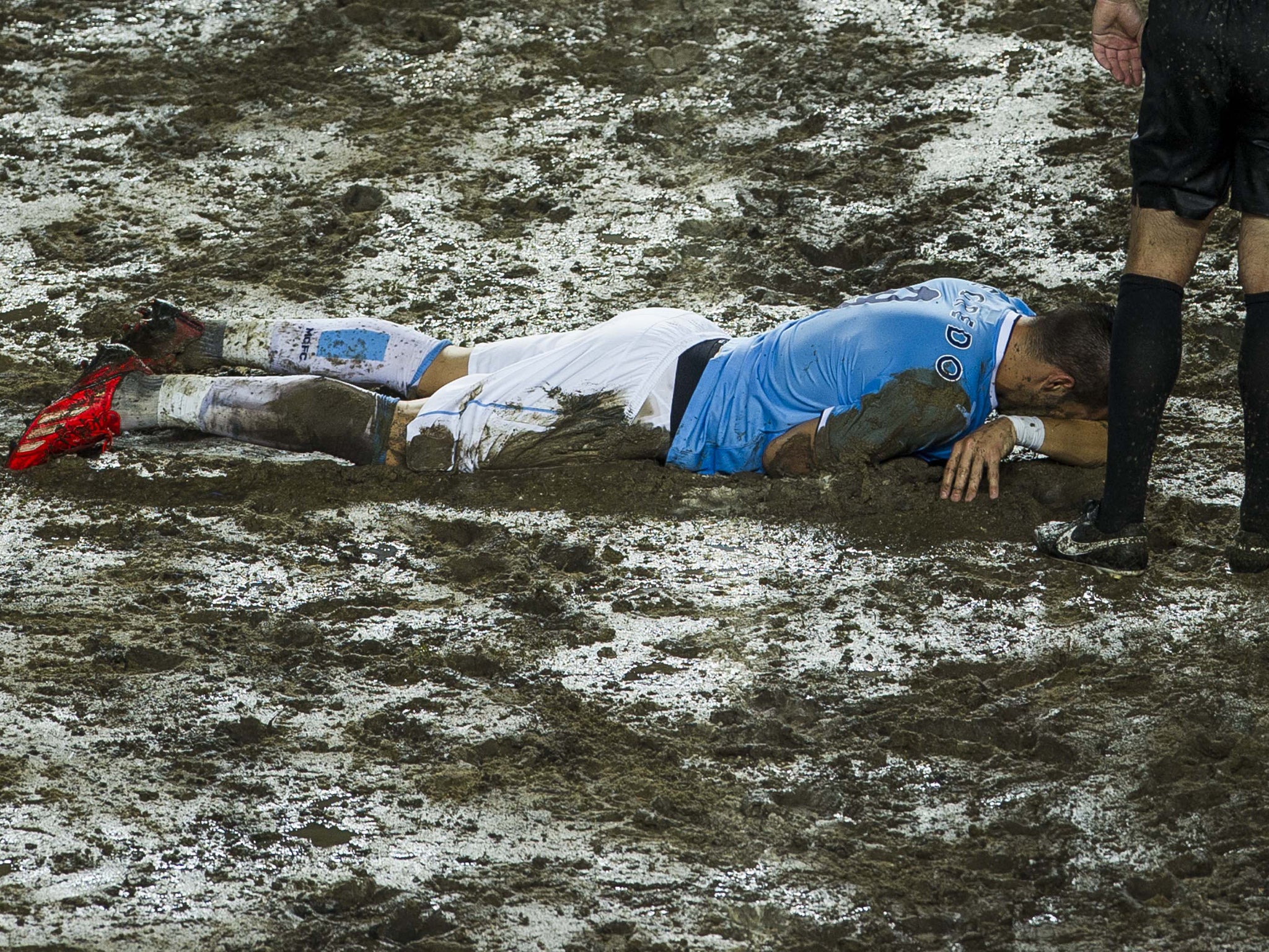 Manchester City's Alvaro Negredo lies face-down in the muddy Hong Kong Stadium pitch