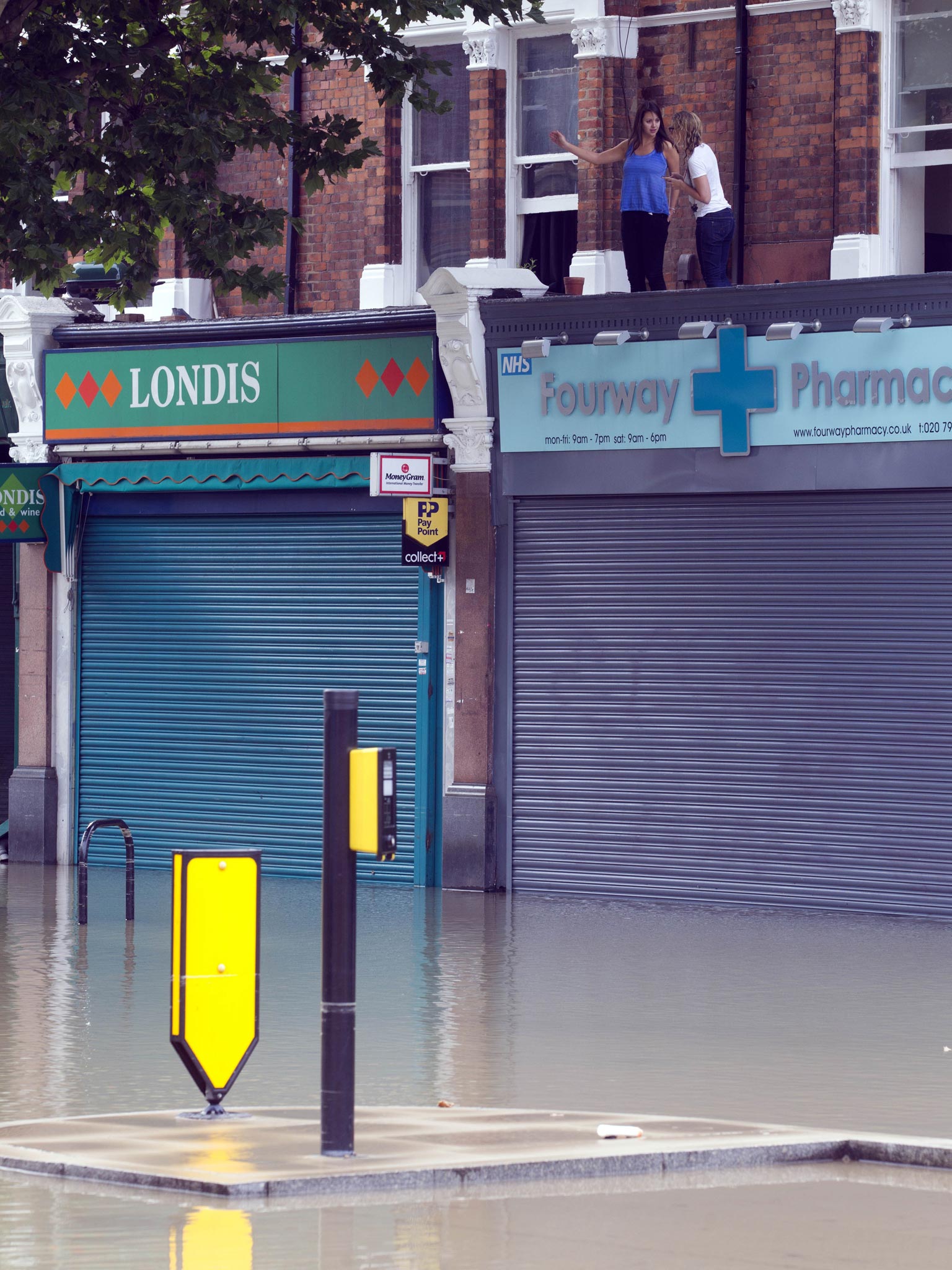 Local residents stand on the rooftops of shops on Half Moon Lane in Herne Hill