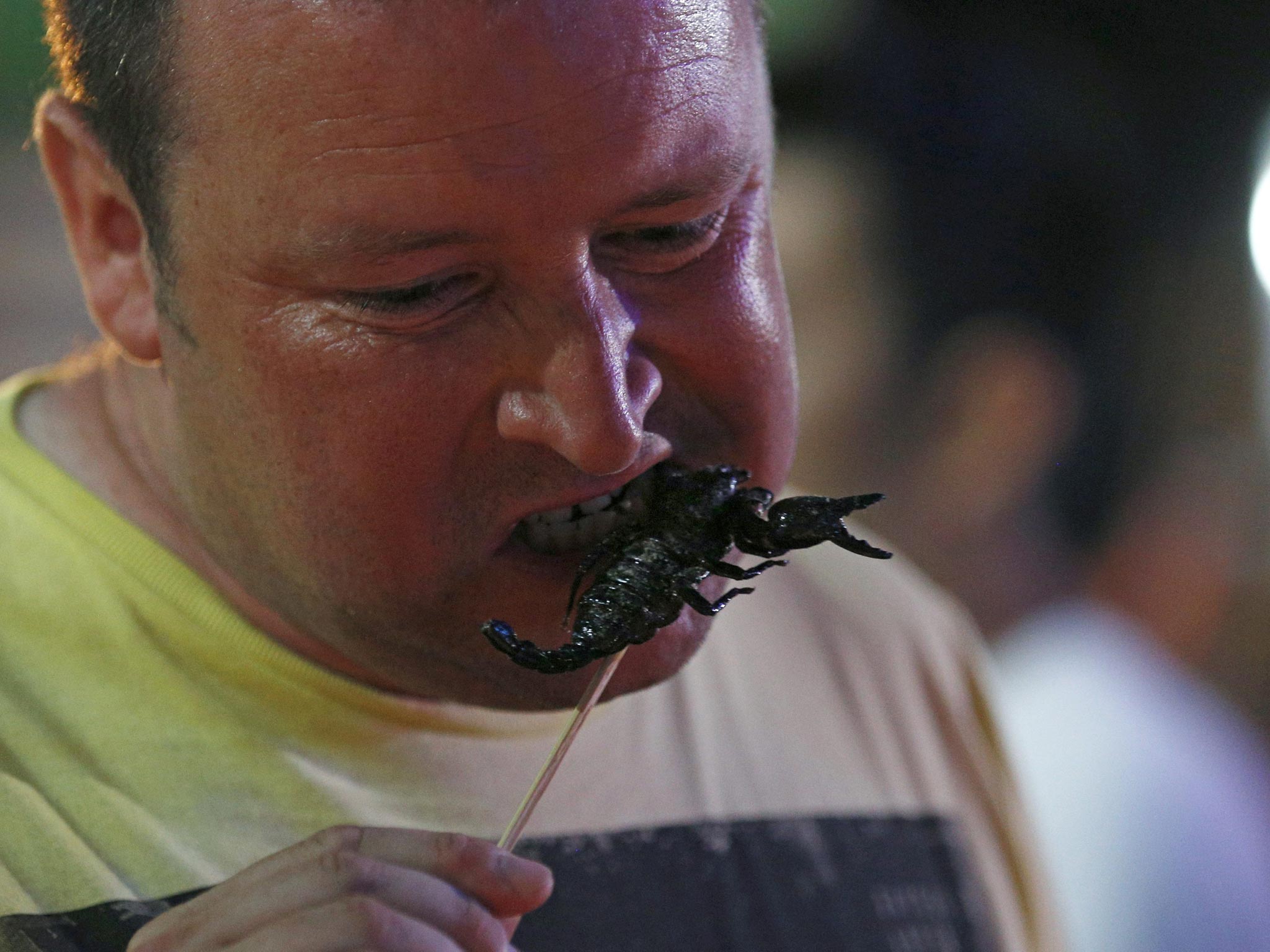 A foreign tourist eats a fried scorpion insect at Khao Sarn road, a spot tourist area in Bangkok, Thailand