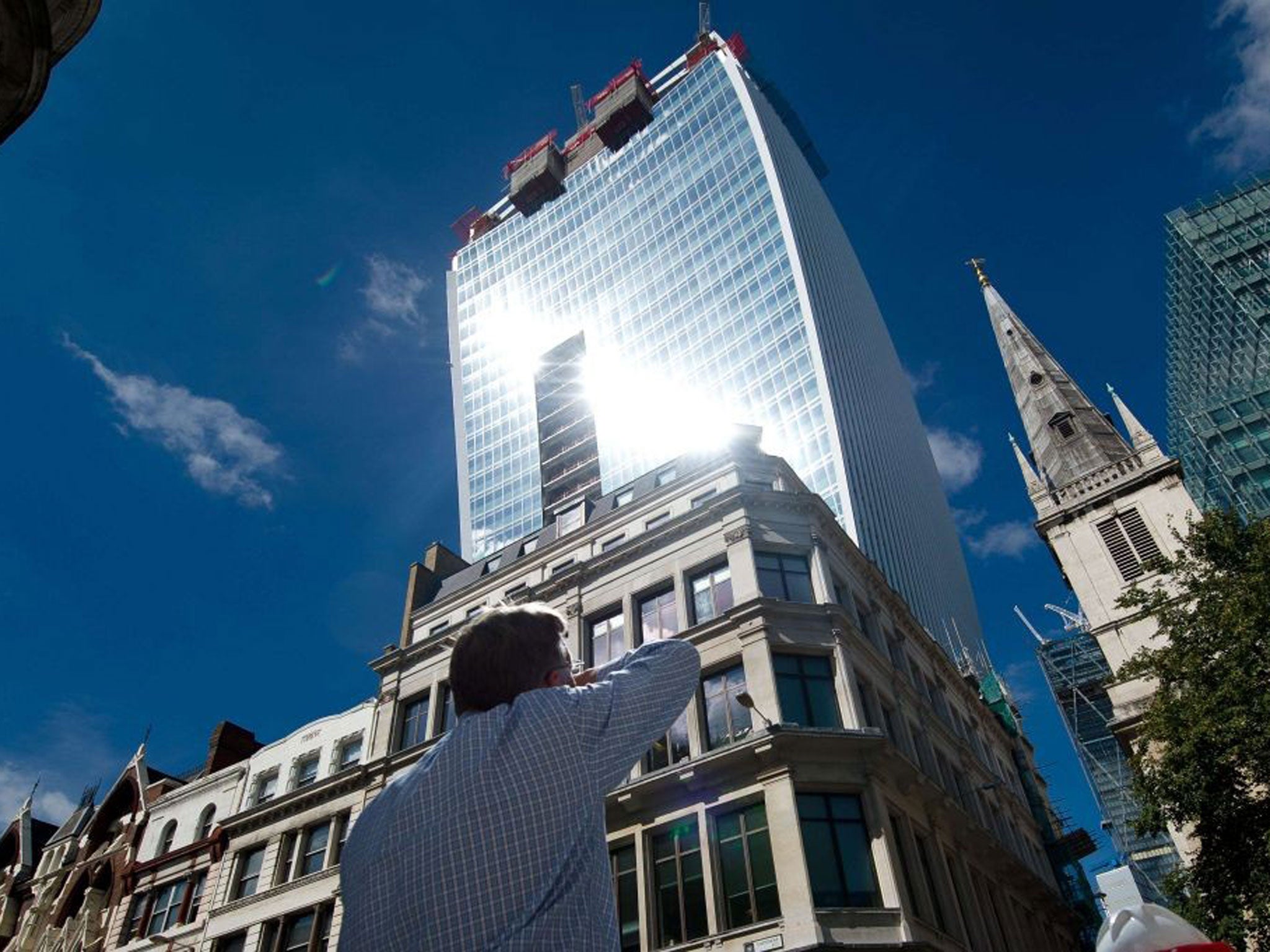 A man reacts to a shaft of intense sunlight reflected from the glass windows of the new "Walkie Talkie" tower in central London