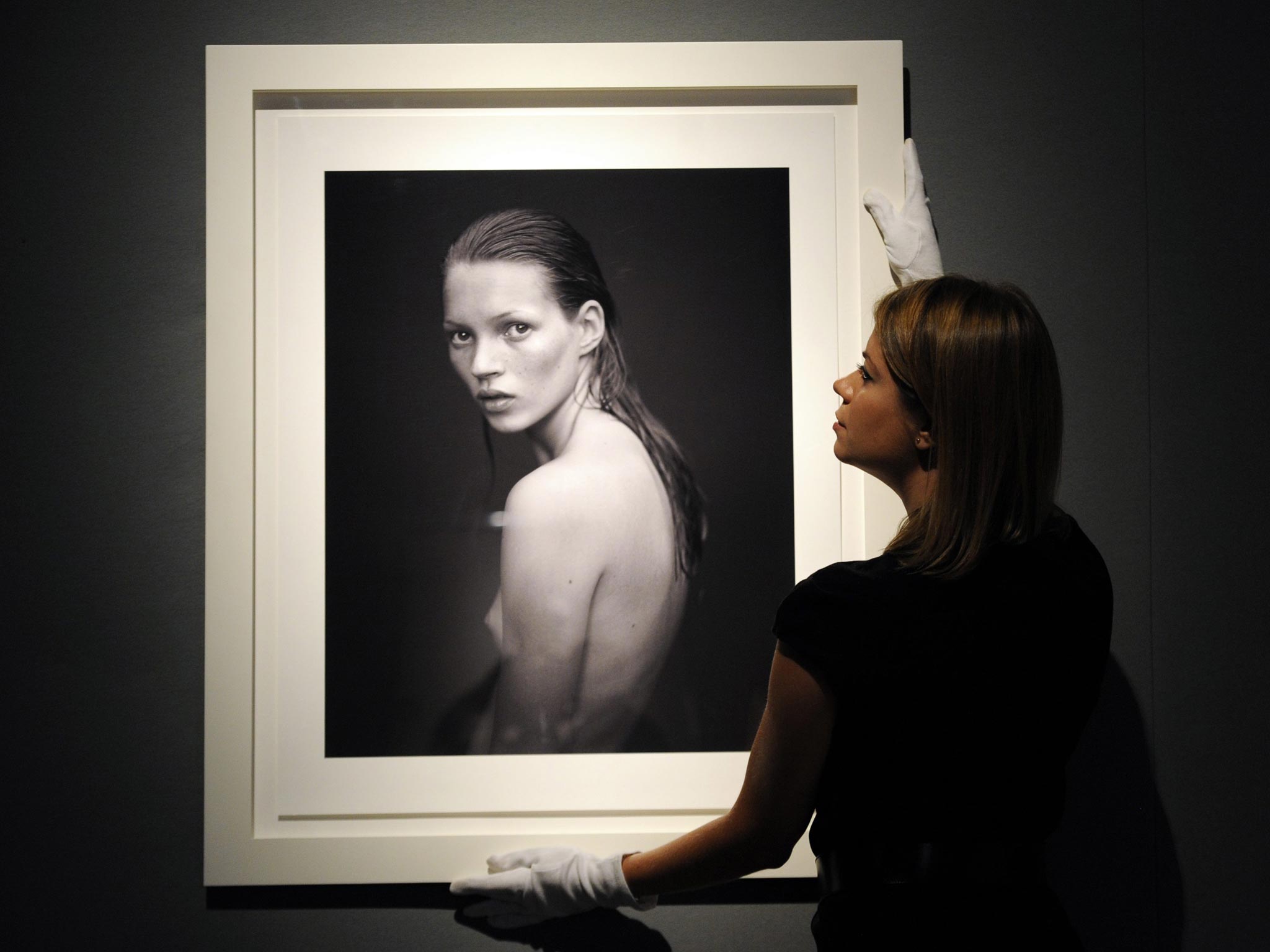 A gallery employee places a photograph of Kate Moss taken for Calvin Klein Obsession campaign in 1993 by US photographer Mario Sorrenti, during a press view of an auction of a selection of works featuring her at Christie's auction house in London