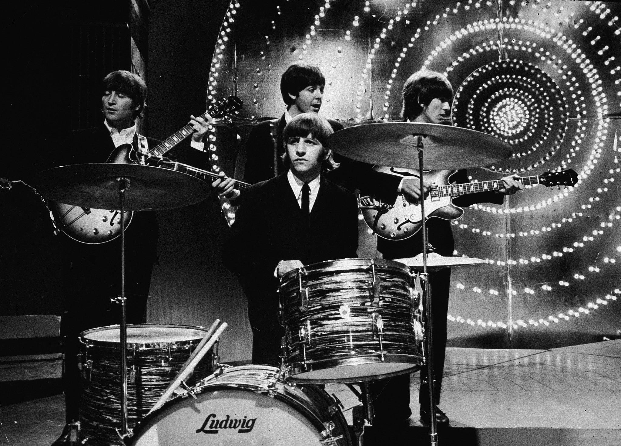 The Beatles perform live on stage in front of a circular lit backdrop at the BBC TV Centre in 1966