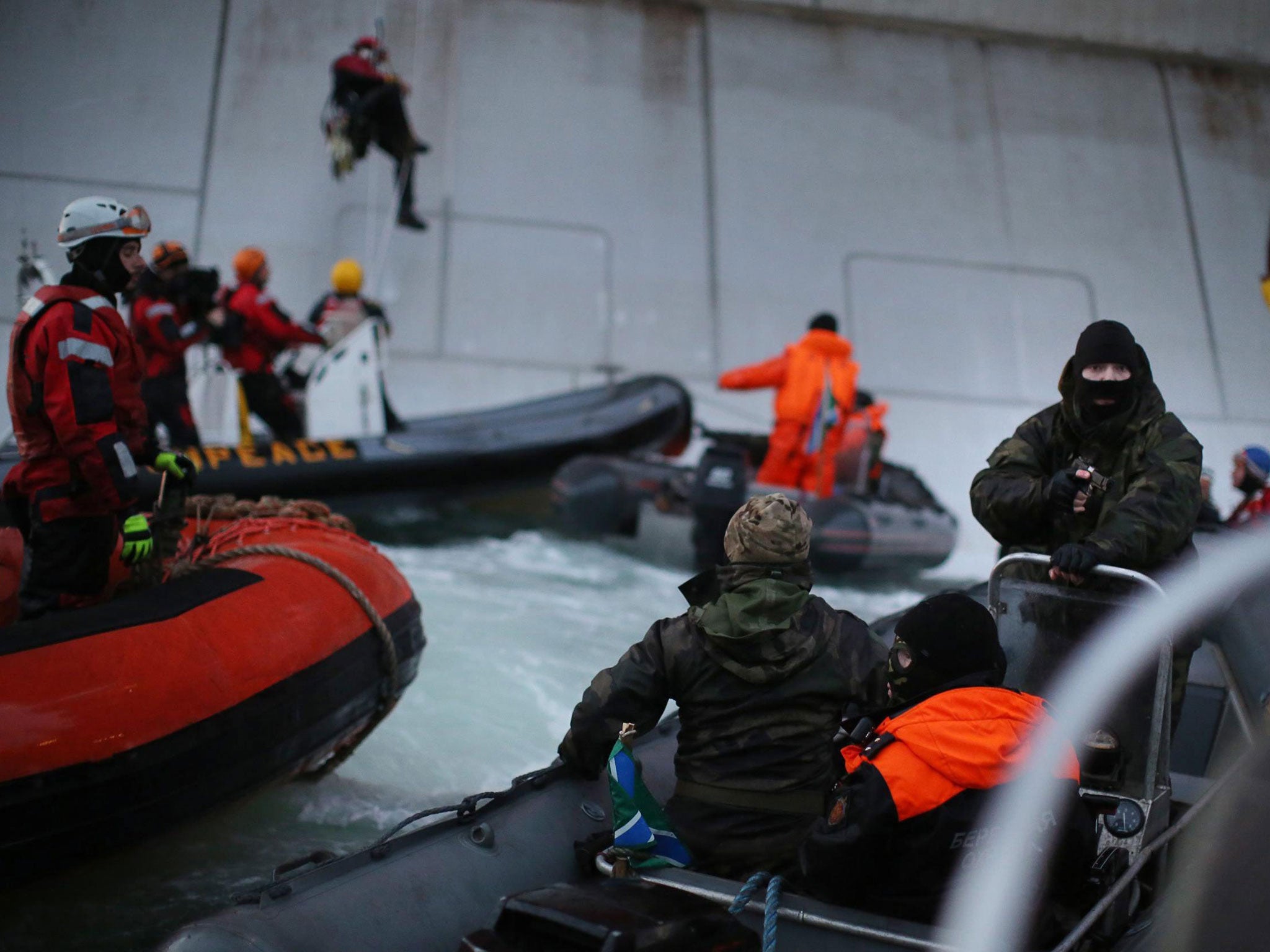 A Russian Coast Guard officer points a gun at a Greenpeace activist as others attempt to climb the Prirazlomnaya oil platform