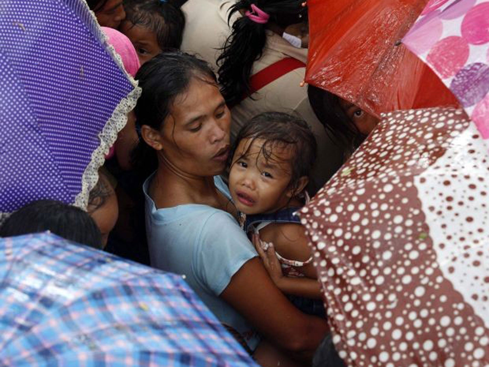 Filipino evacuees use their umbrellas to shelter from the rain, waiting for food relief in Sagbayan town