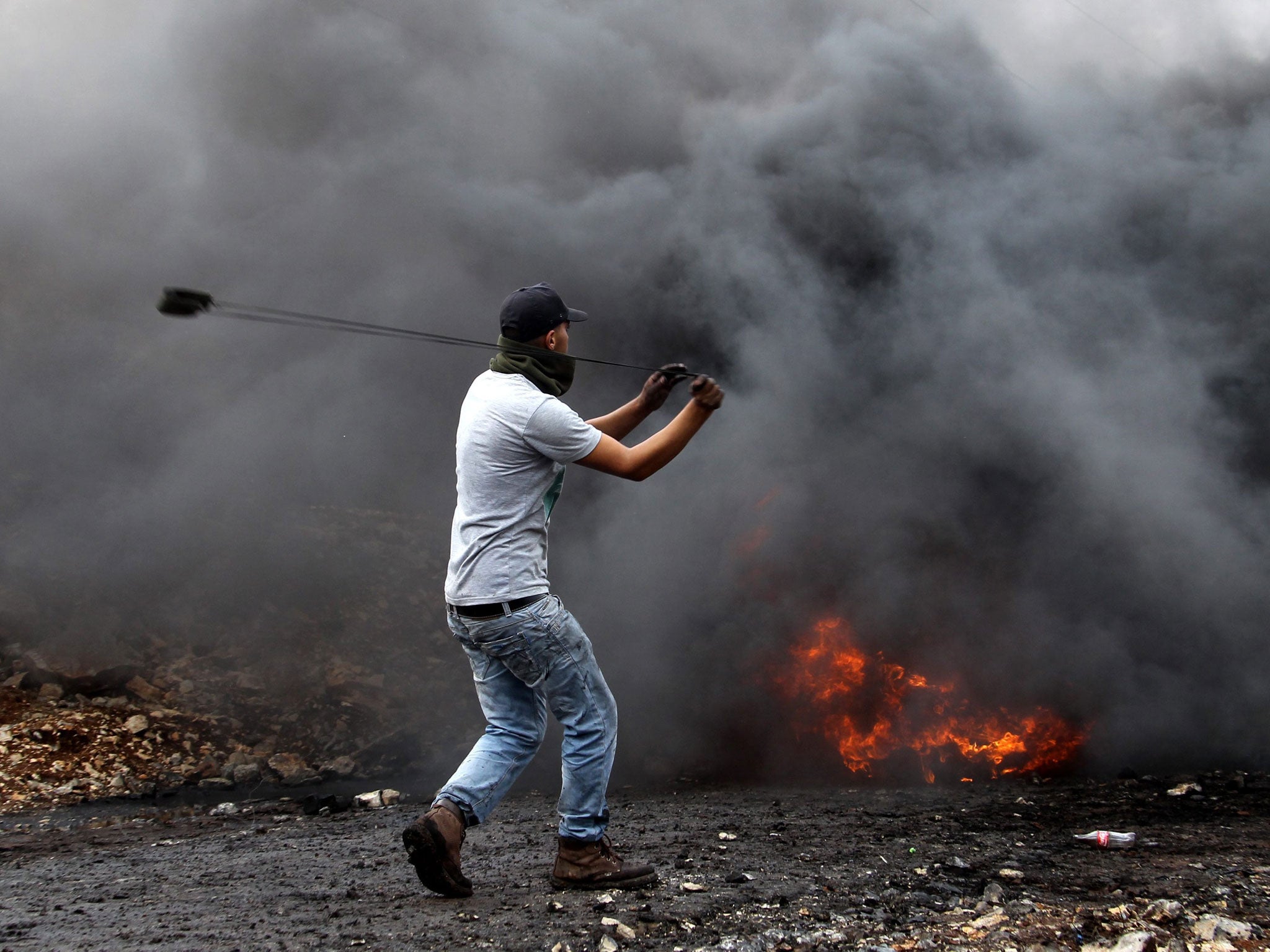 A Palestinian protester uses a sling to throw stones at Israeli soldiers