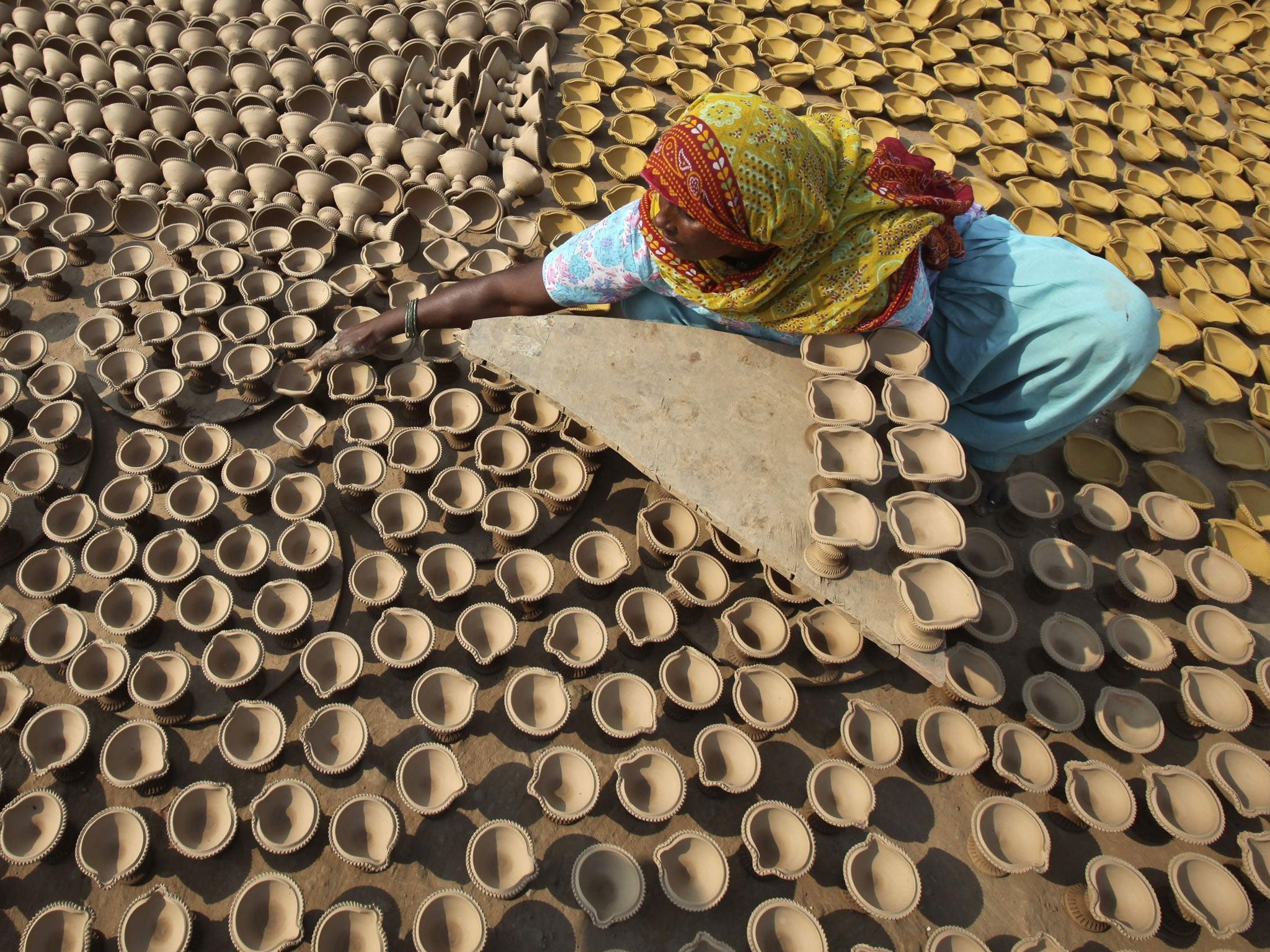 A woman puts out earthen lamps to dry in the sun in preparation for Diwali.