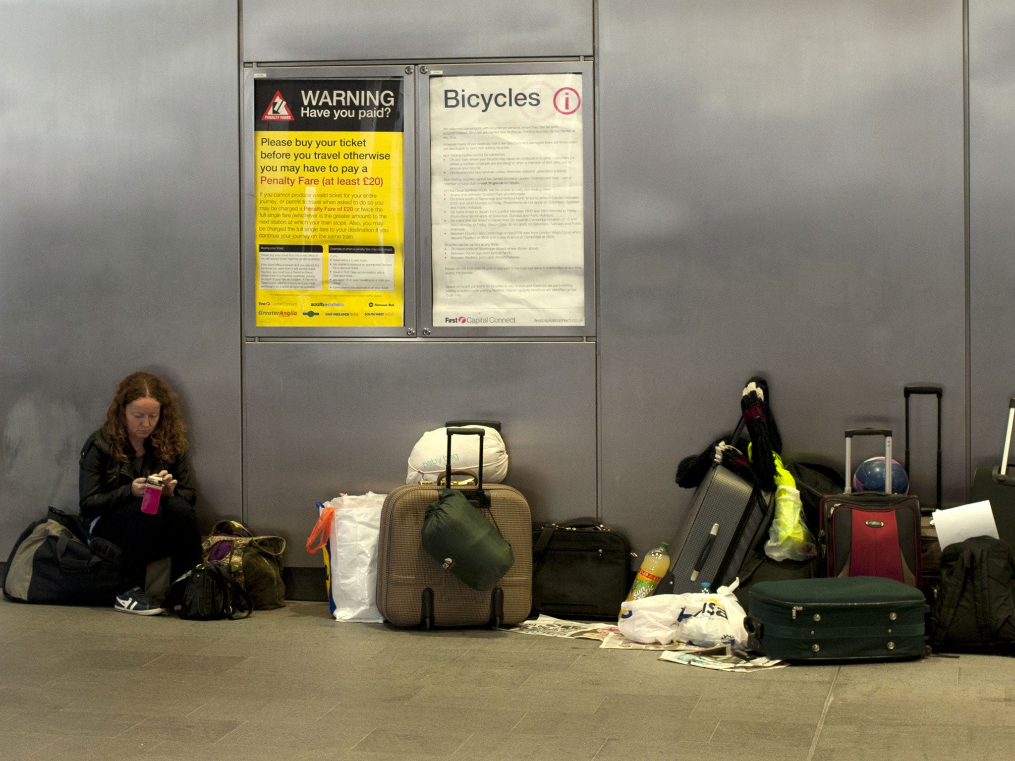 A passenger sits beside luggage on the concourse after trains were cancelled at Kings Cross train station