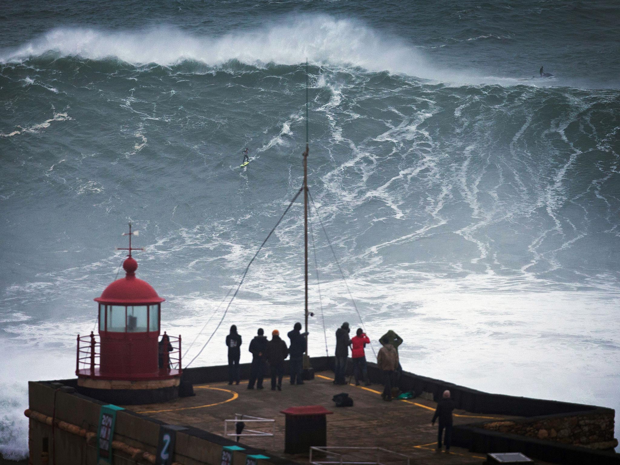 People watch an unidentified surfer ride a big wave at the Praia do Norte, north beach, at the fishing village of Nazare in Portugal's Atlantic coast