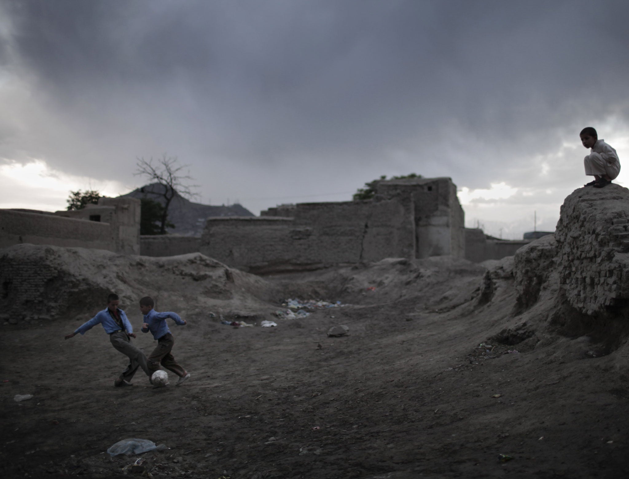 Two Afghan boys play soccer near ruins as the rain approaches at nightfall in the old part of Kabul, on April 10, 2010.