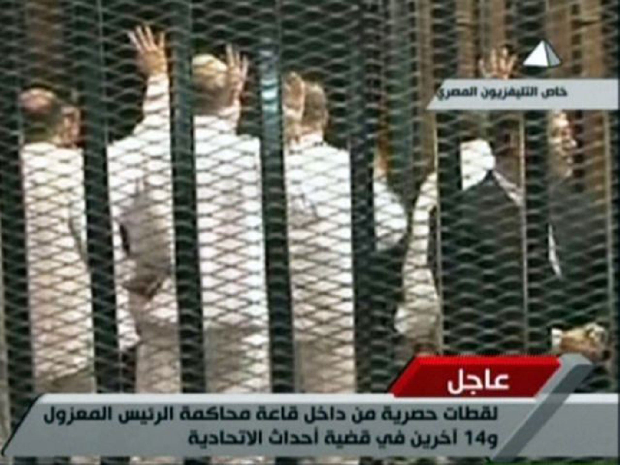 An image grab taken from Egyptian state TV shows Morsi (R) in court along with 14 co-defendants. He stands apart after refusing to wear the prescribed prison uniform, as his fellow Muslim Brotherhood members hold up the four-fingered salute that has become a symbol of resistance to the summer's military coup