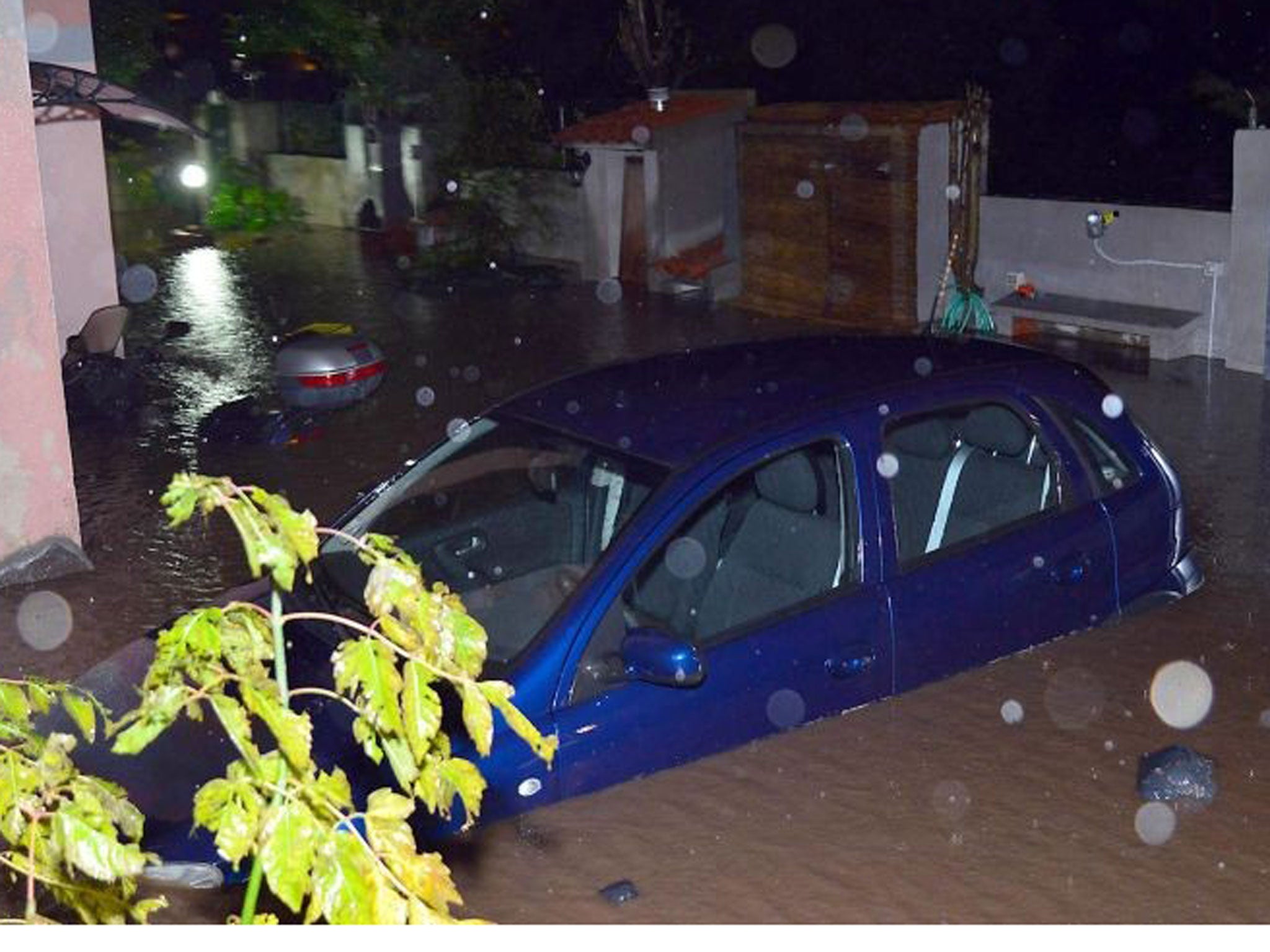 A car and a motorscooter stand in floodwater near a house that was completely flooded following the heavy storm, near Olbia