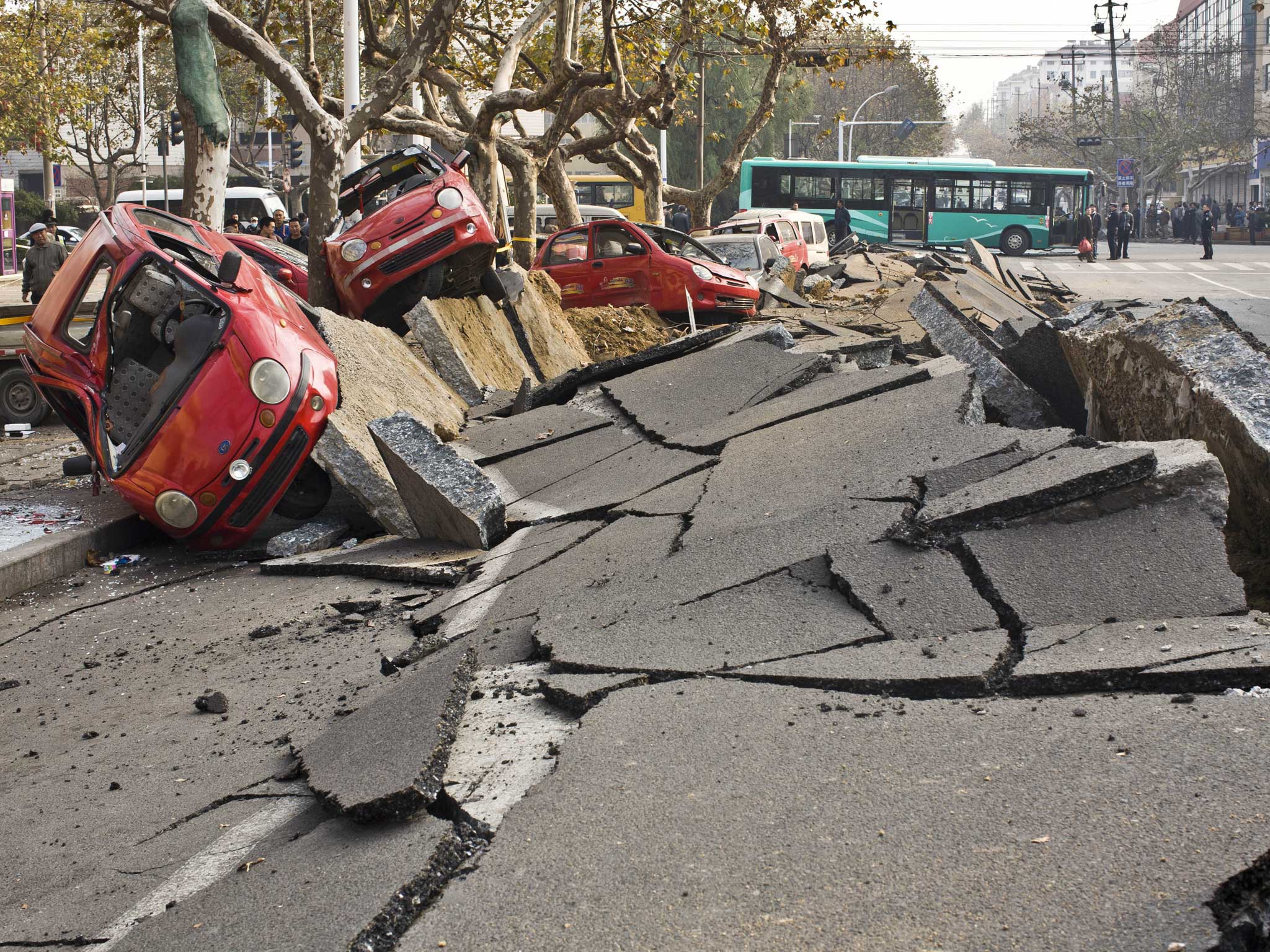 Damaged vehicles lie by a street after an oil pipeline exploded, ripping roads apart, turning cars over and sending thick black smoke billowing over the city of Qingdao