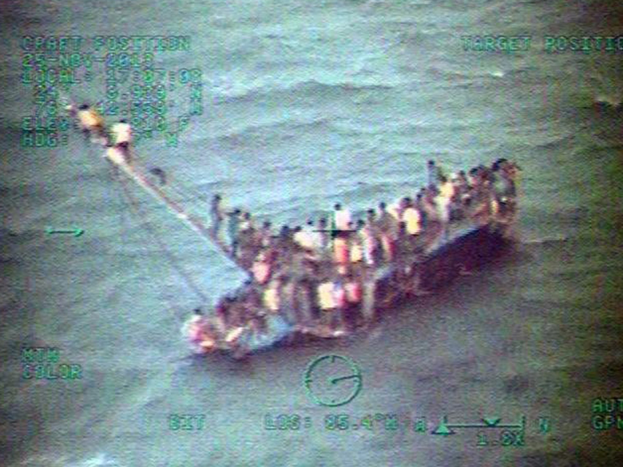 A handout picture made available by the US Coast Guard and taken from a Coast Guard helicopter shows some 100 Haitians sitting on the hull and mast of a sail freighter after it grounded and capsized off the coast of the Bahamas