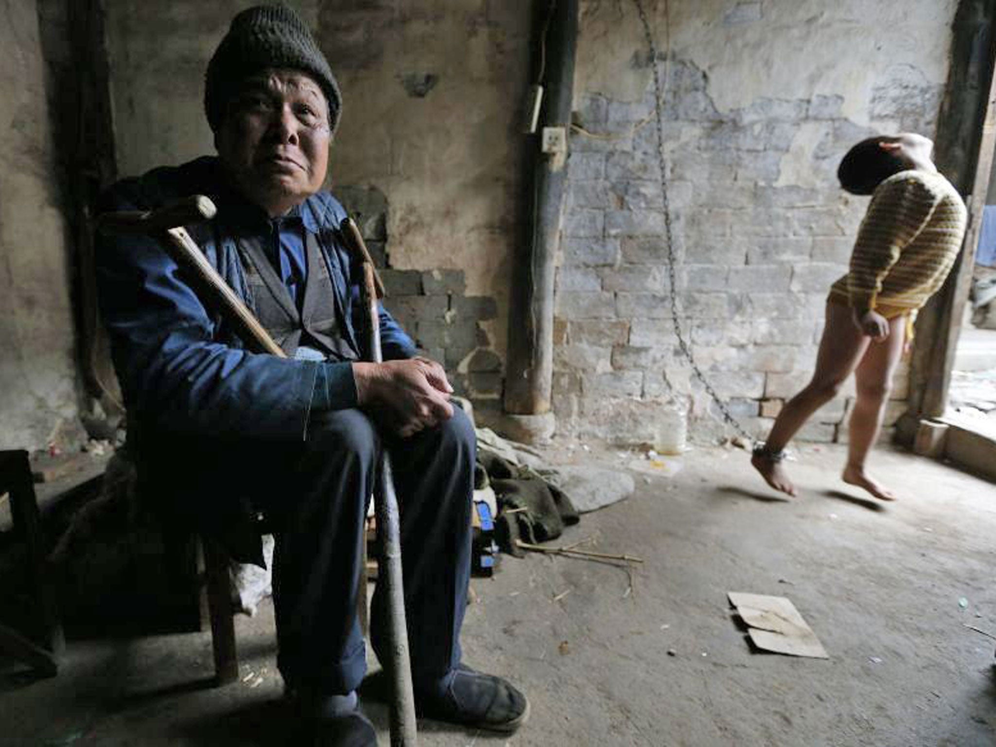 He Zili, 11, is seen chained to a wall as his grandfather sits next to him at their home in Zhejiang province