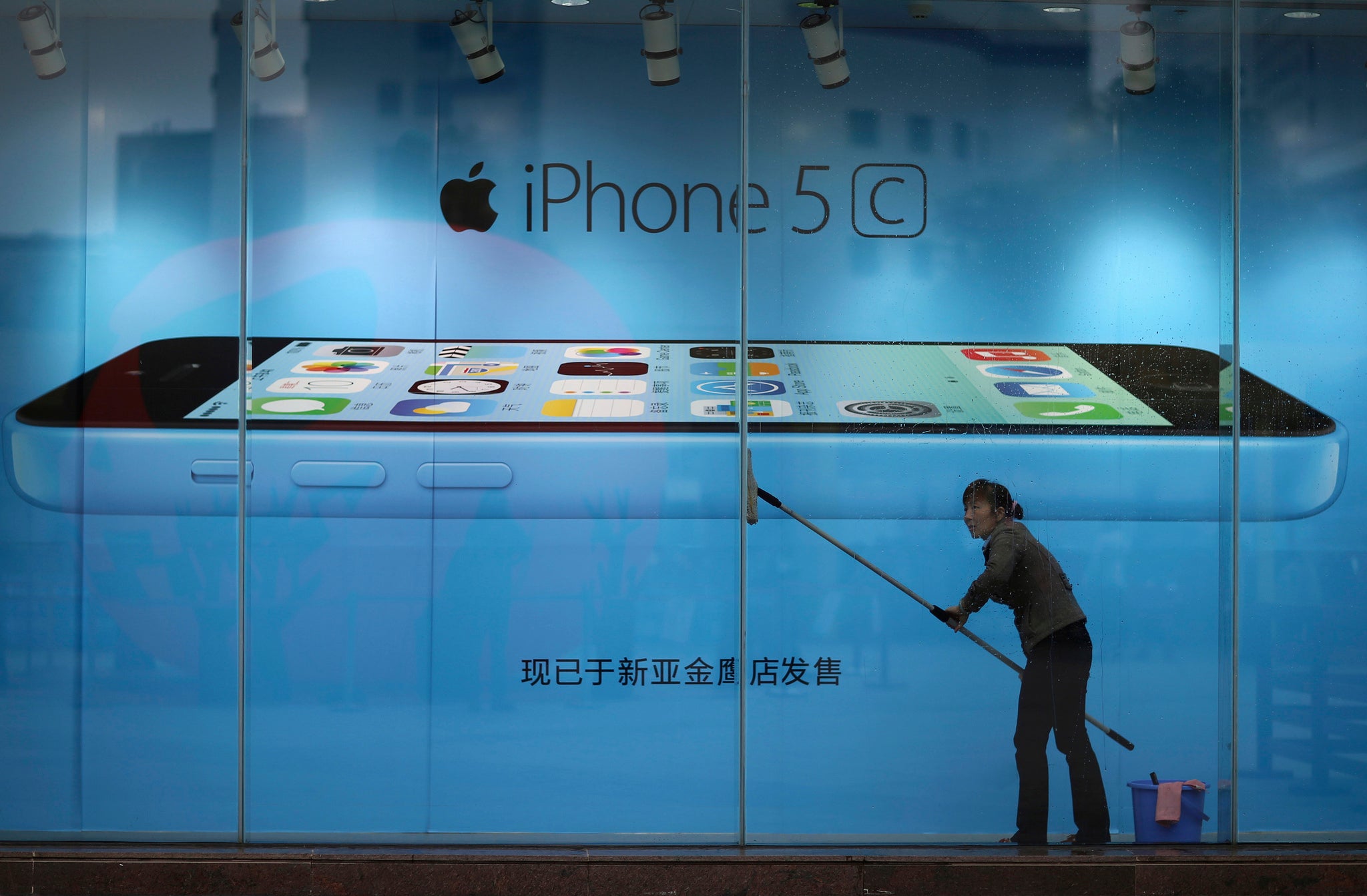 A worker cleans glass in front of an iPhone 5C advertisement at an apple store in Kunming, Yunnan province, China.