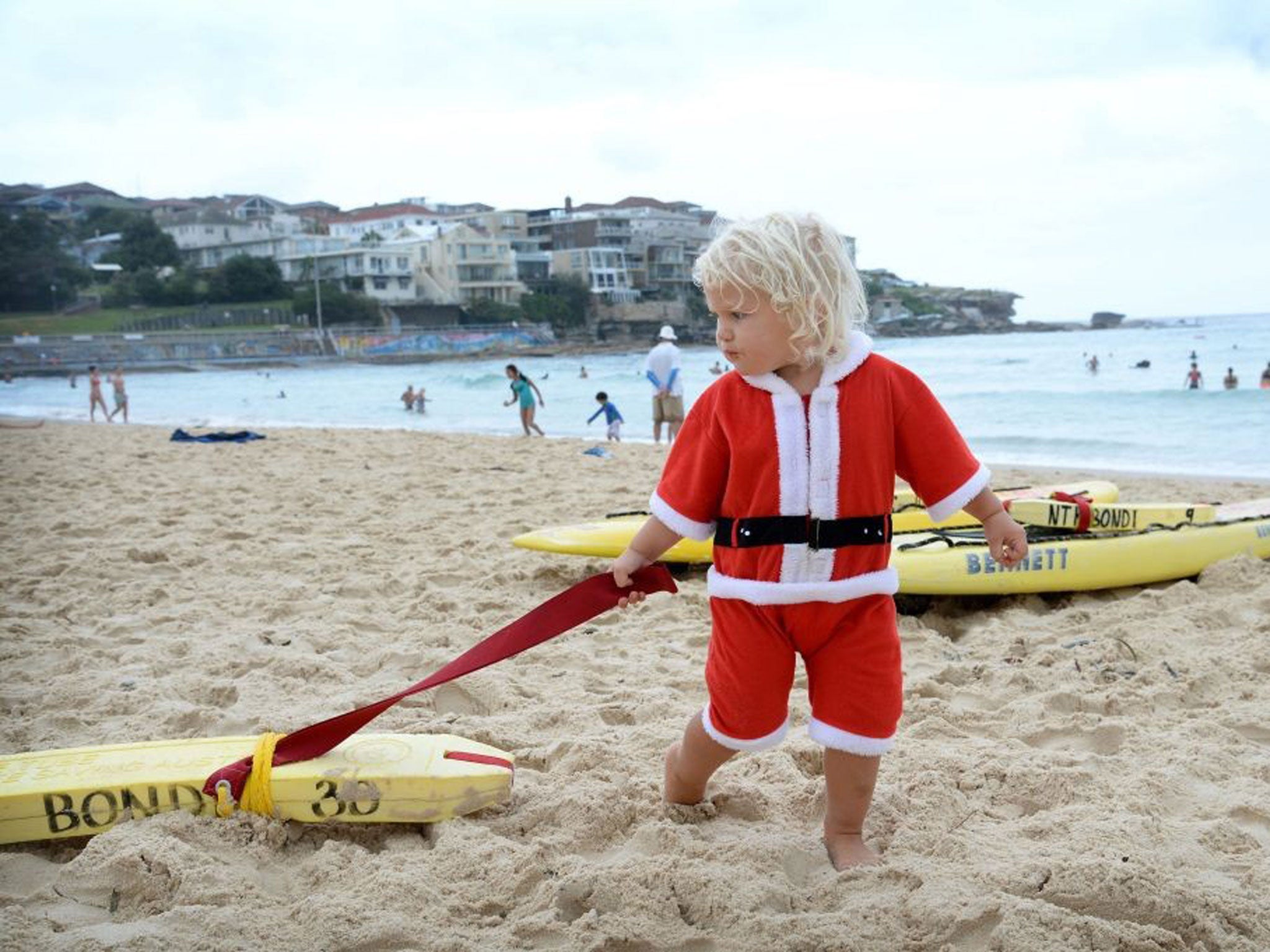 A 2-year-old boy dressed as Santa plays on surfboards at Bondi beach in Sydney, as Sydney-siders celebrated Christmas Day under wet and cloudy, but warm conditions