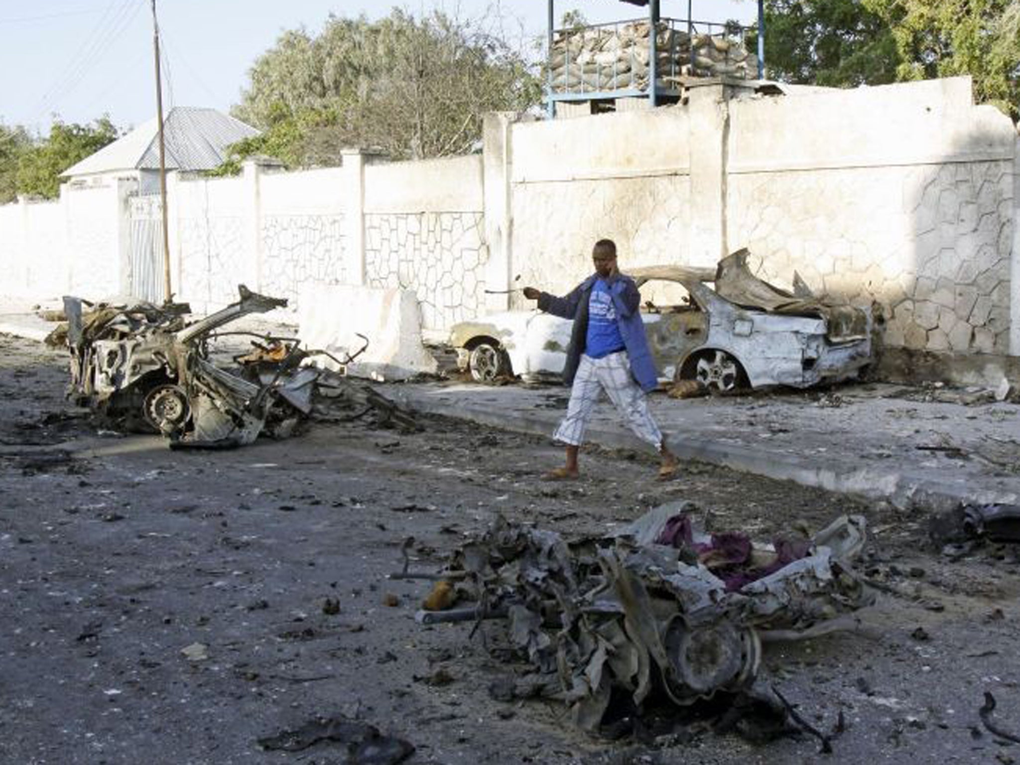 A man walks near the wreckage of cars after bombs went off at the gate of a hotel in Mogadishu