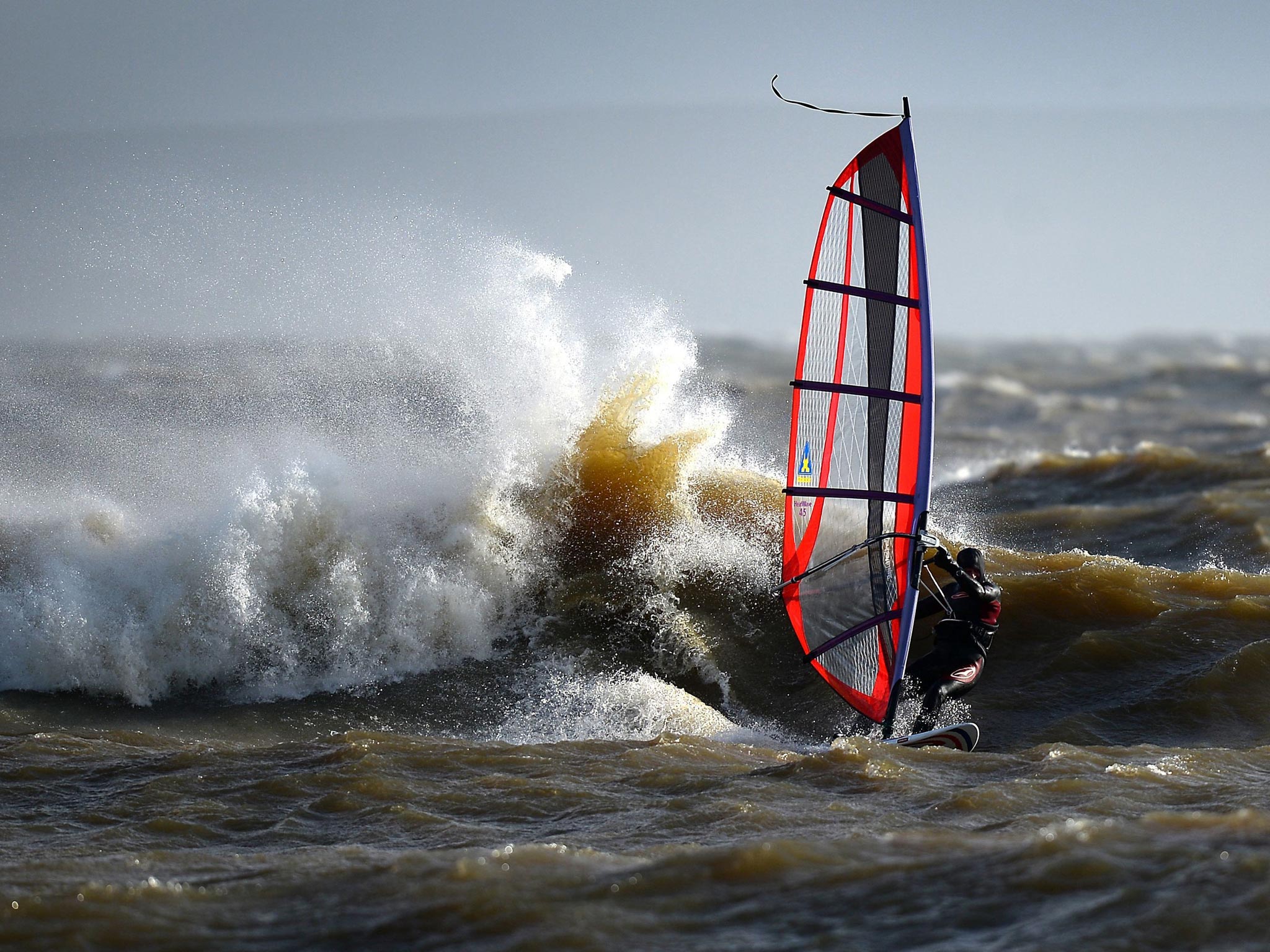 A windsurfer enjoys the stormy conditions in the sea off of Mudeford beach in Dorset, as heavy rain and strong winds sweep across the country.