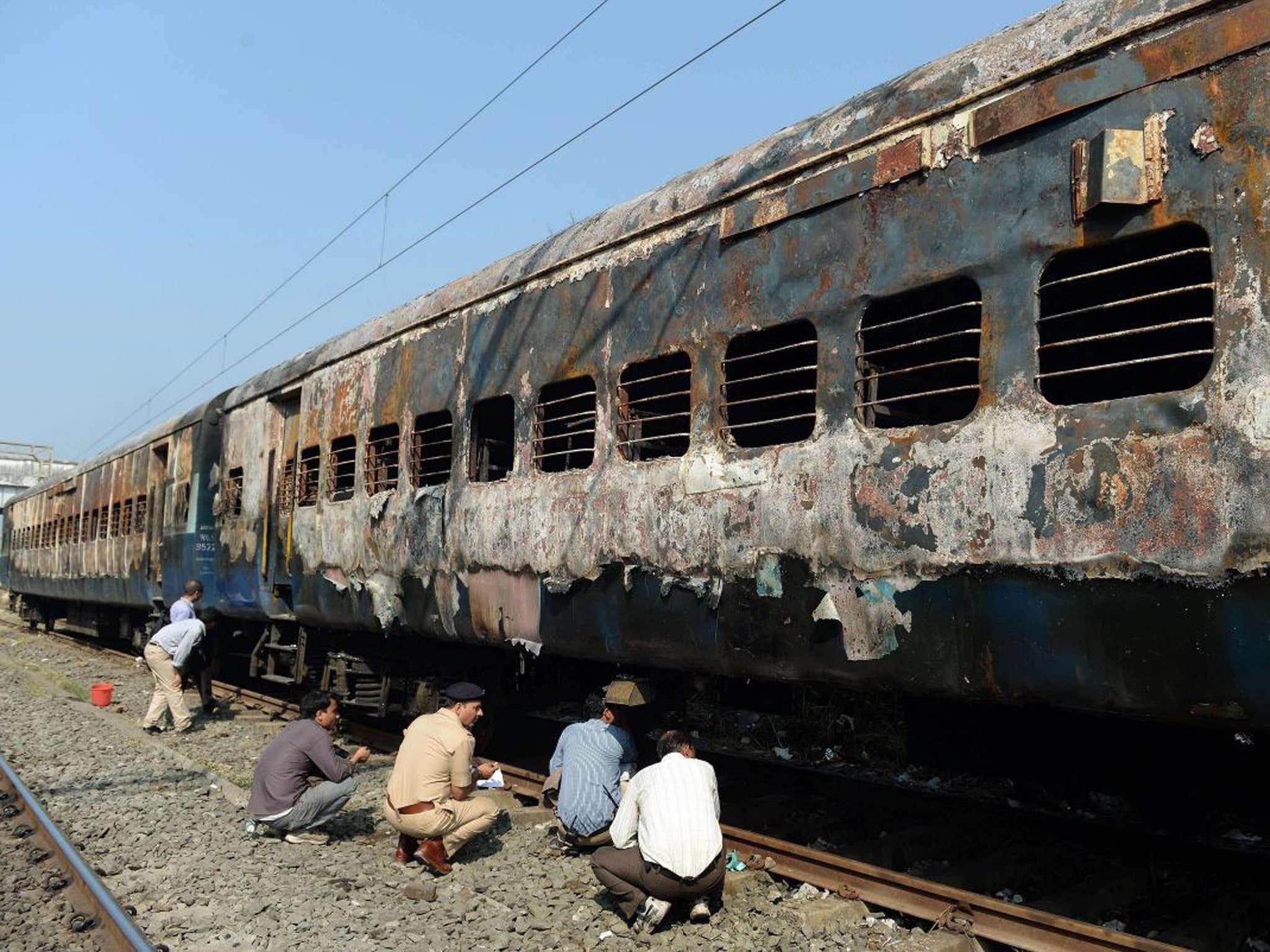 Indian railway and police officials inspect the burnt carriages of the long distance passenger train near Dahanu railway station