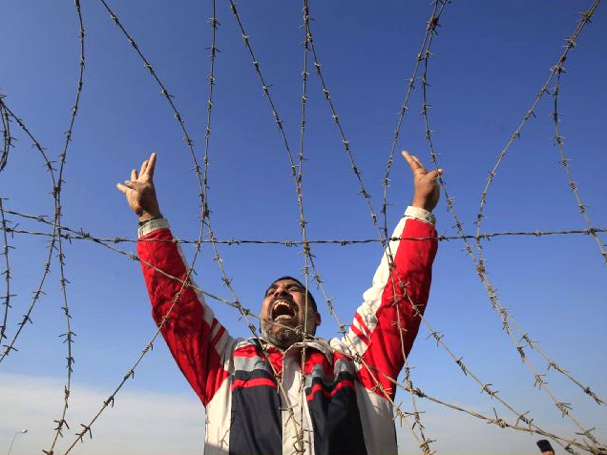 A supporter of the Muslim Brotherhood and ousted Egyptian President Mohamed Mursi shouts slogans against the military and interior ministry, while gesturing with four fingers, during a protest in front of riot police outside a police academy, on the outsk