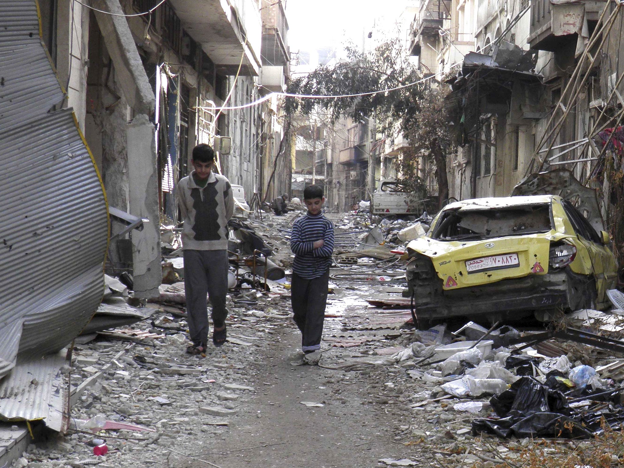 Boys walk along a street past damaged buildings and vehicles in the besieged area of Homs