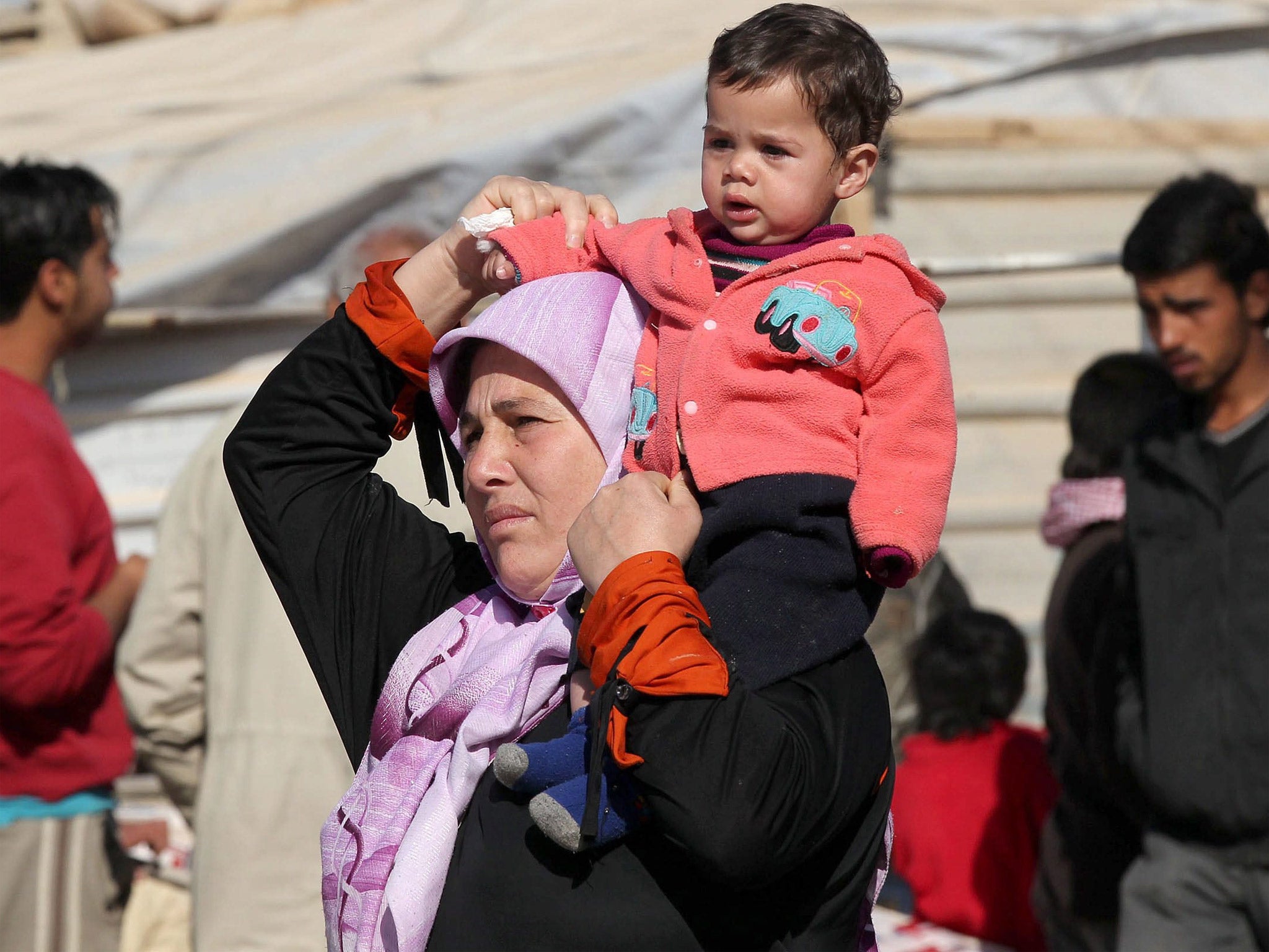 A Syrian woman carries a child on her shoulder at a refugee camp in Jordan (Getty)