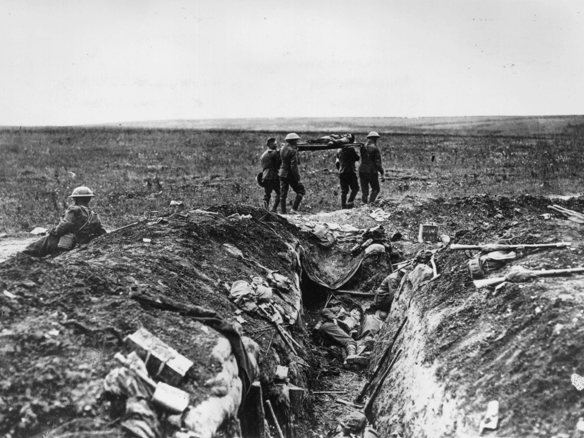 1915: A wounded British soldier is stretchered back to camp past a carnage-strewn trench, during the World War I