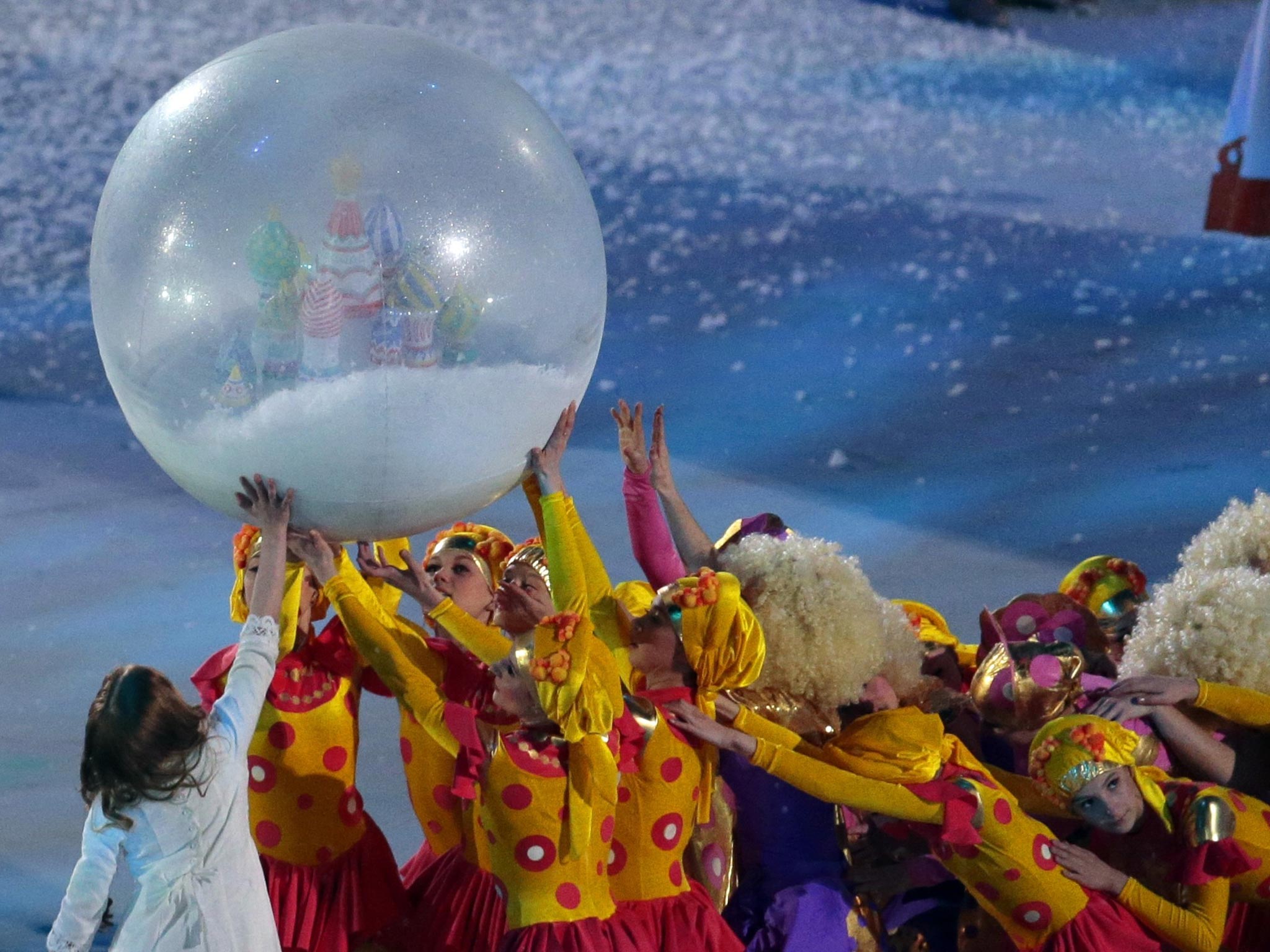 Young dancers in red and yellow costumes hold up a giant balloon during a snow scene