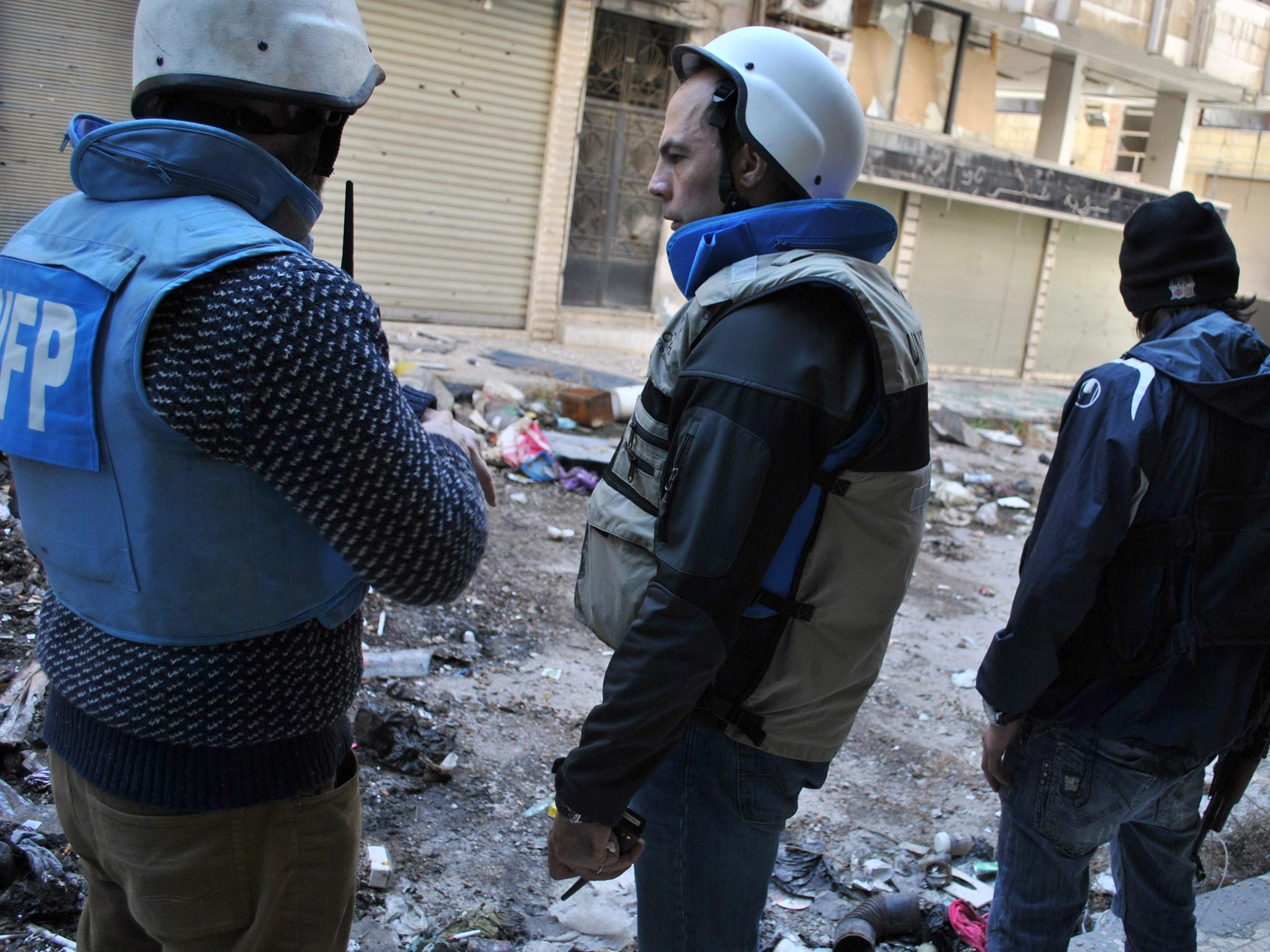 Members of a United Nations and Syria's Red Crescent convoy stand in a street after entering a besieged district of the central city of Homs