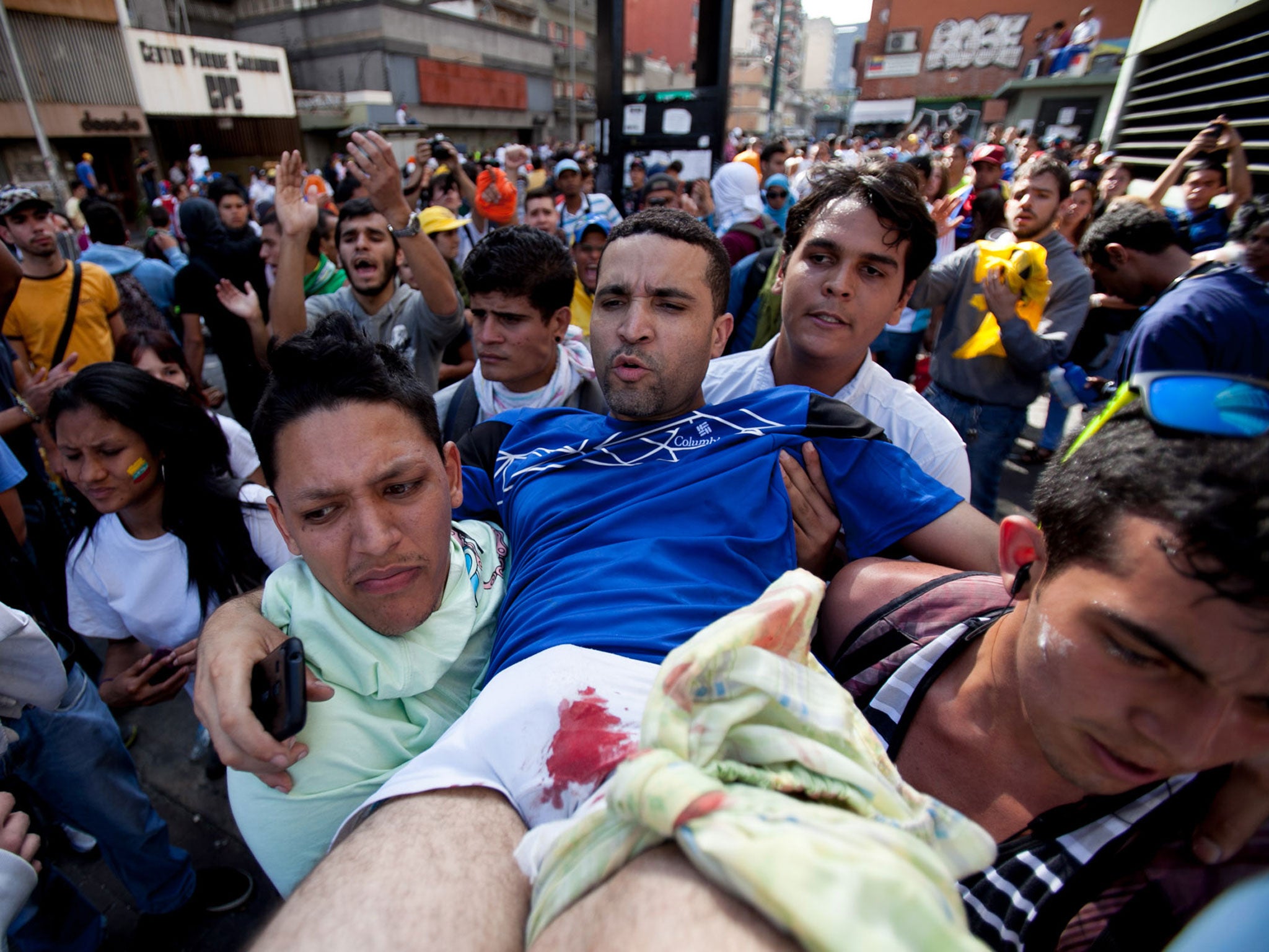 A demonstrator with a gun shot wound to his left leg is carried to safety after clashes broke out in Caracas