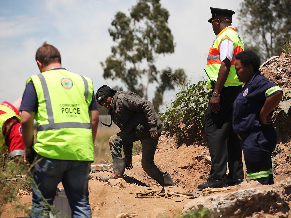 Police stand at the access site of an illegal gold mine in Benoni, in the East Rand, on February 17, 2014, as they rescue ten more trapped miners after already pulling out eleven the day before, who remained underground fearing arrest. A total of 22 illeg