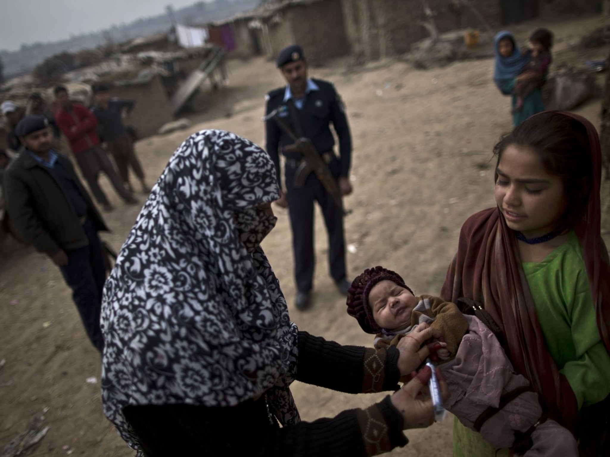 A Pakistani health worker marks the finger of an Afghan refugee child held by her elder sister, after giving her a polio vaccine, on the outskirts of Islamabad, Pakistan, on 26 February 2014