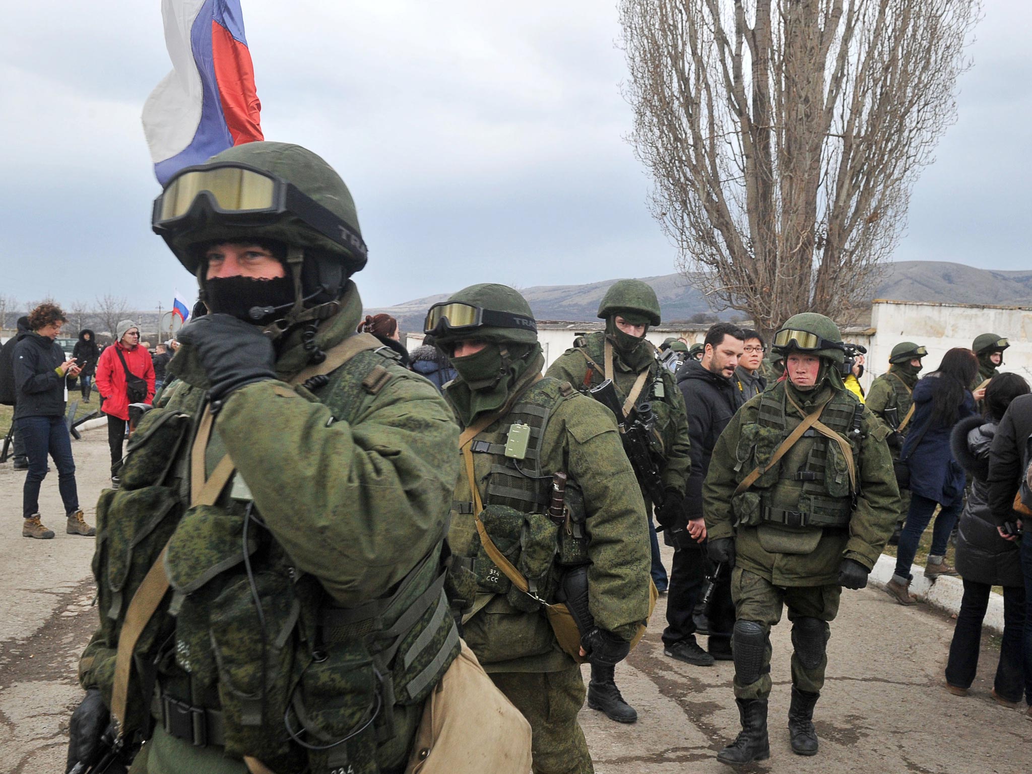 A man holds a Russian flag as armed men in military fatigues block access to a Ukrainian border guards base