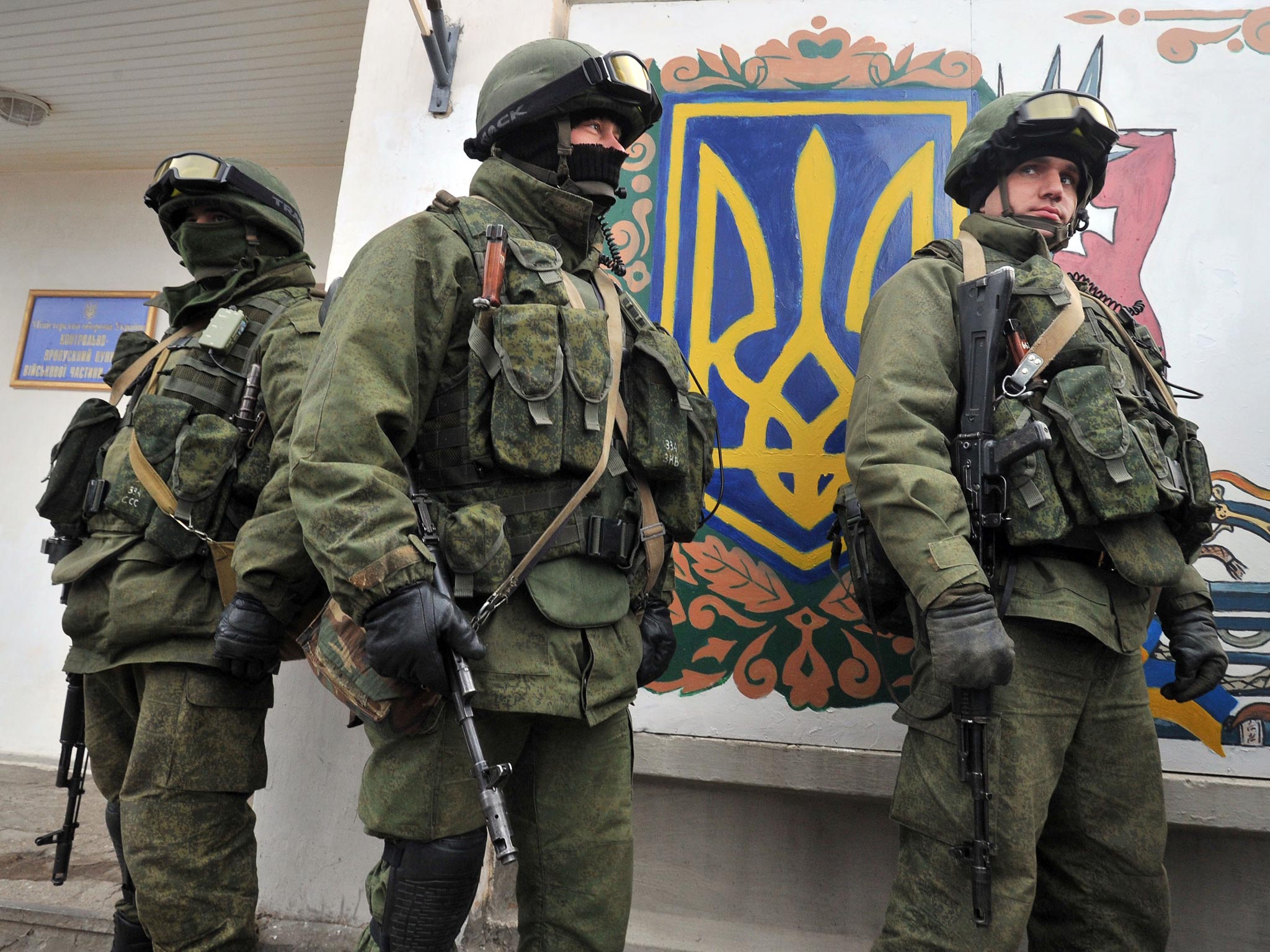 Armed men in military fatigues stand near a painted Ukrainian coat of arms symbol as they block access to a Ukrainian border guards base not far from the village of Perevalne near Simferopol