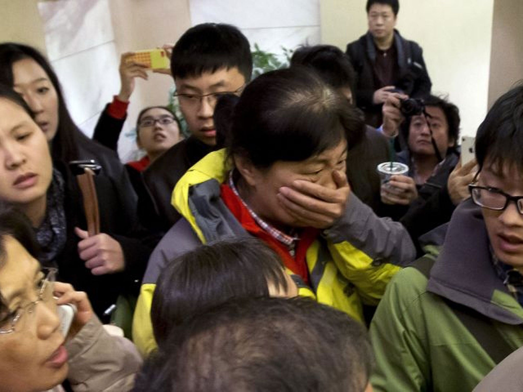 A woman surrounded by media covers her mouth on her arrival at a hotel which is prepared for relatives or friends of passengers aboard a missing airplane, in Beijing, China