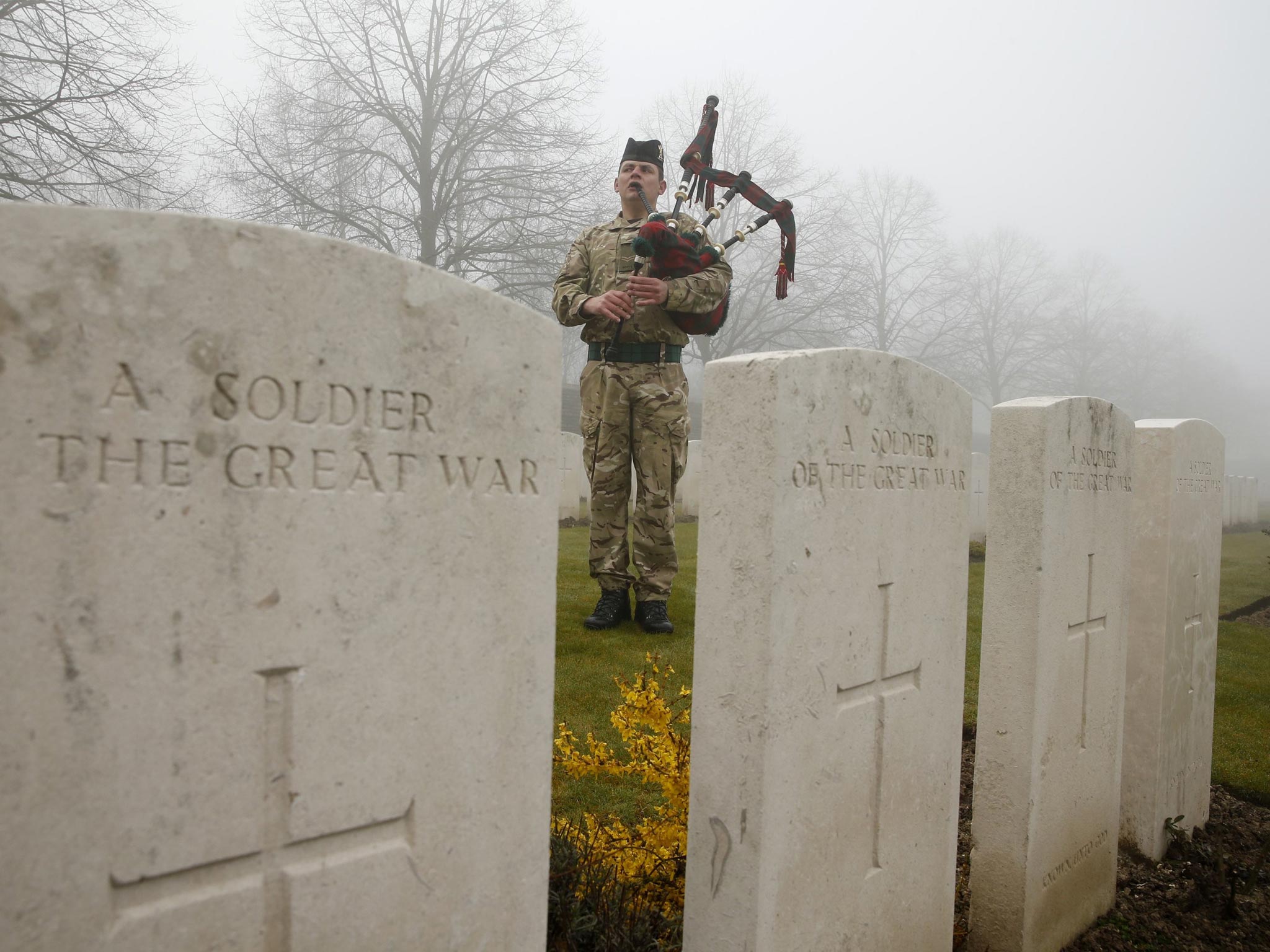 Corporal Stuart Gillies of the 2nd Battalion of the Royal Regiment of Scotland plays bagpipes amongst tombstones at a WWI memorial