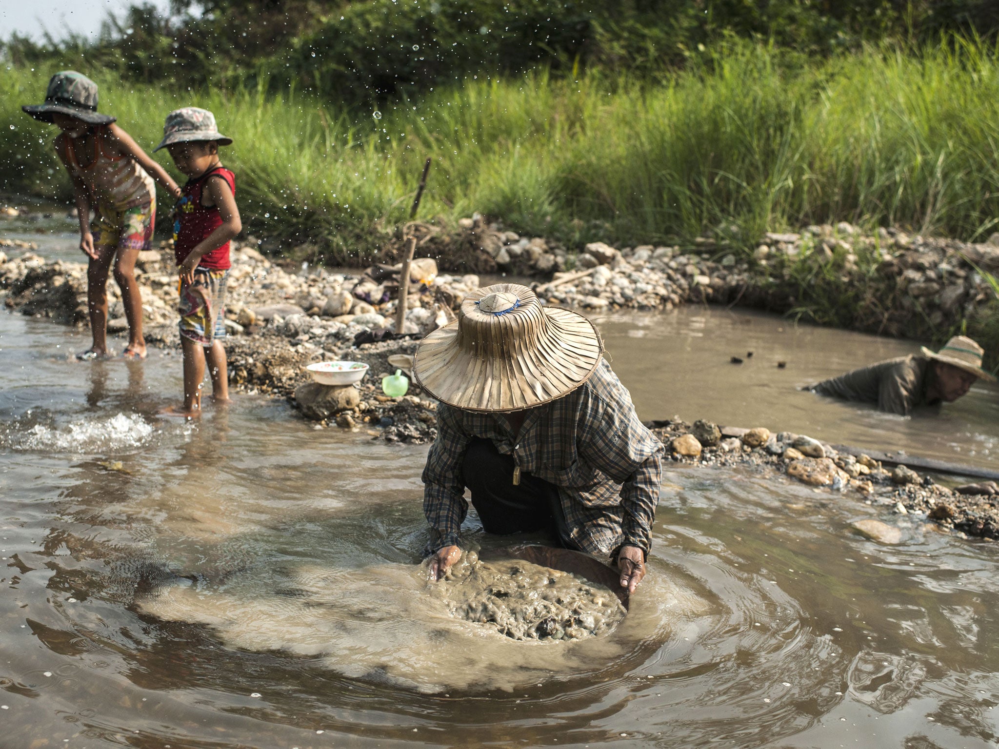 Petong (C) and Hue (R) look for gold as their children play in the water in Lampang