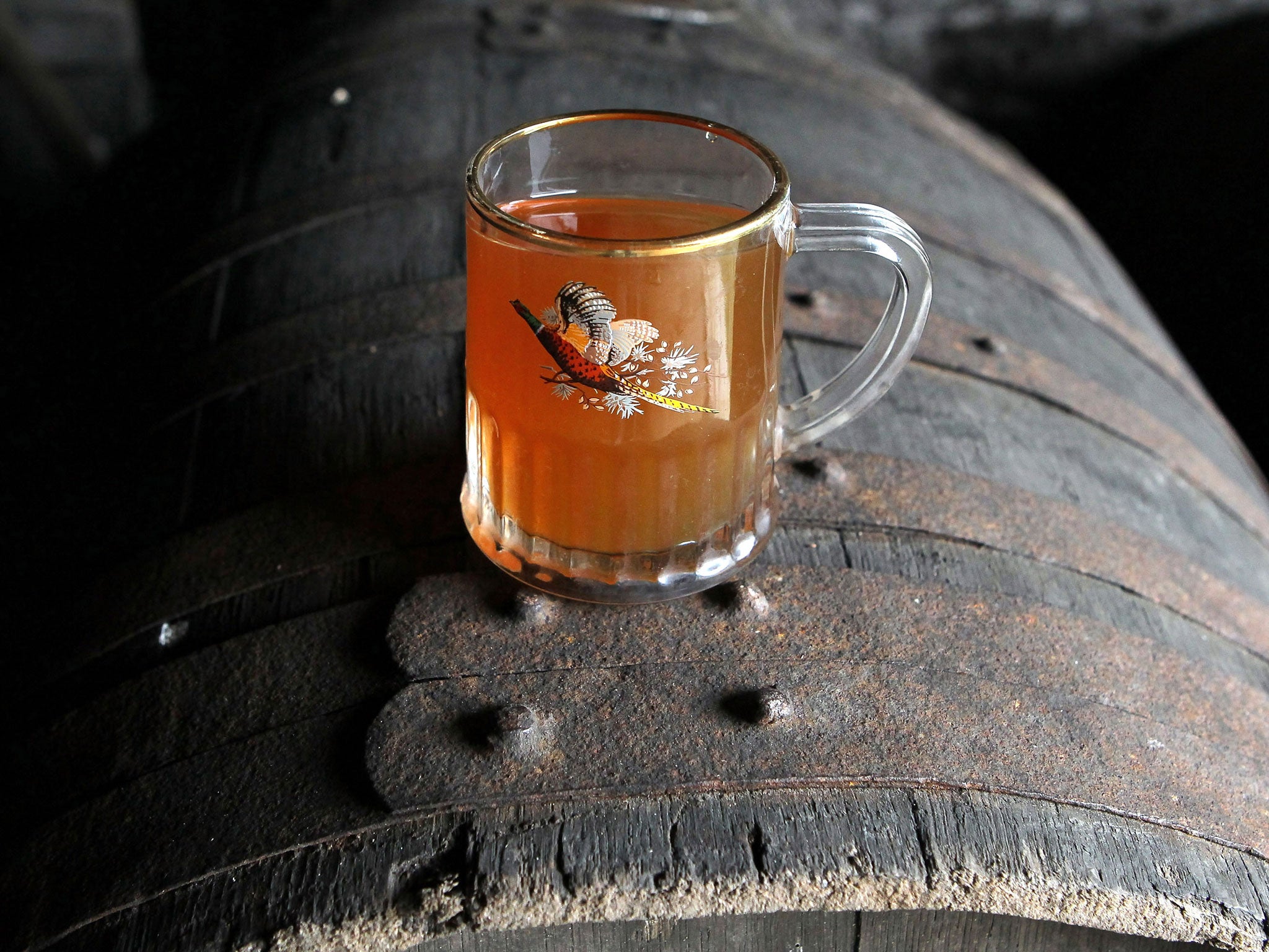 A glass of cider is placed on a wooden barrell