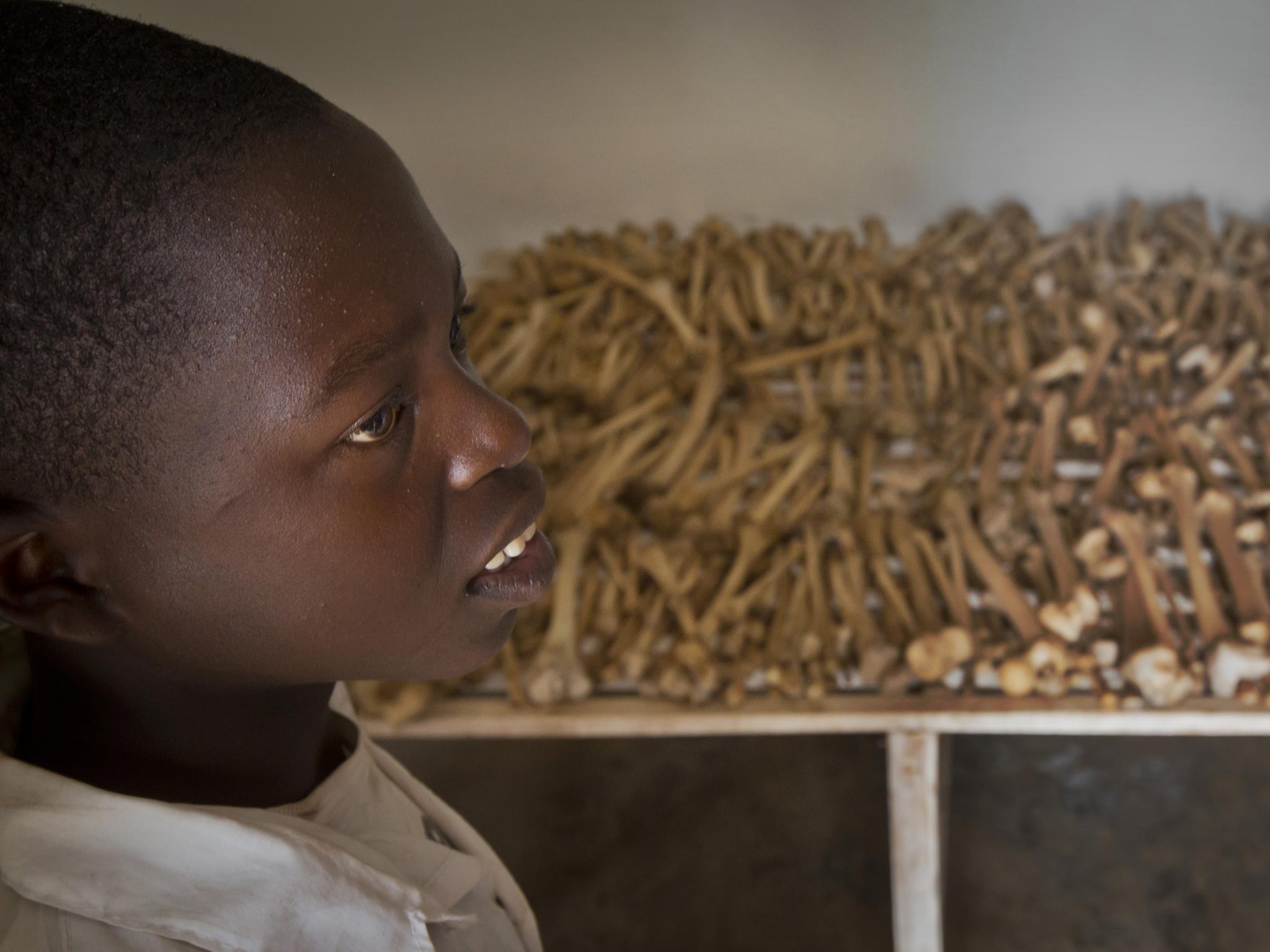 Nikeyimana Obadia, 12, who lives nearby, stands by rows of human bones that form a memorial to those who died in the redbrick church that was the scene of a massacre during the 1994 genocide, in the village of Nyarubuye, eastern Rwanda