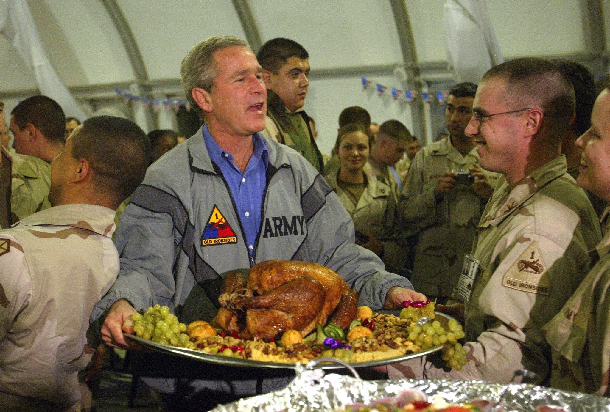 President George W. Bush carry a platter of turkey and fixings as he visits U.S. troops for Thanksgiving in Baghdad on 27 November 2003