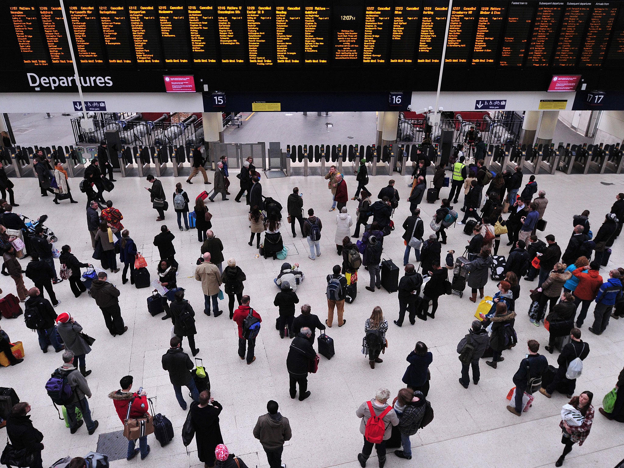 People wait with their luggage by the departure boards in Waterloo train station in central London as disruption to rail services continues on December 24, 2013.