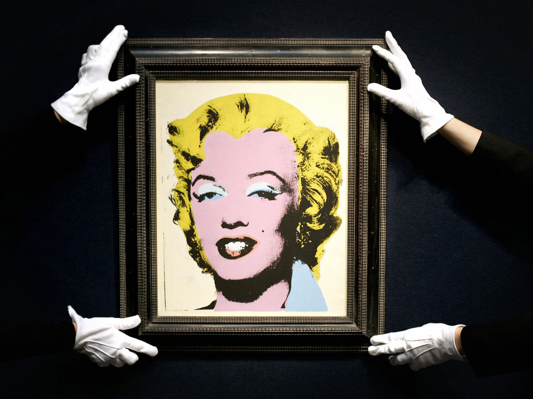 Two Christie's employees hold Andy Warhol's painting 'Lemon Marilyn' - his 'White Marilyn' sold for $41m on Tuesday