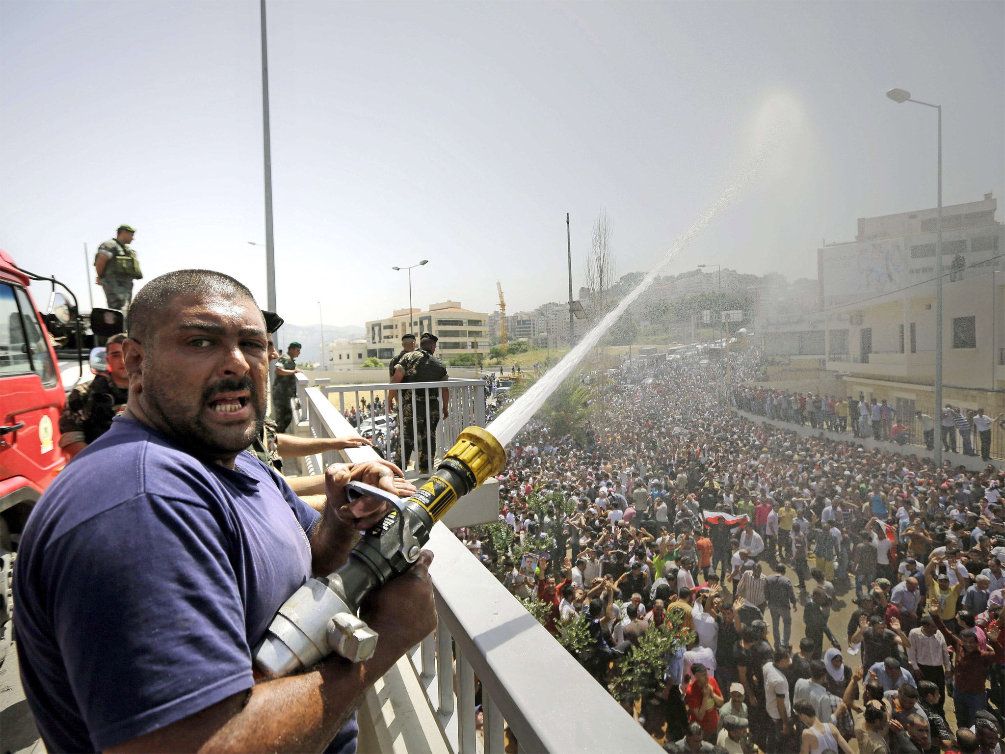 A fireman sprays water on Syrian expatriates living in Lebanon to keep them cool, as they arrive to cast their ballots in their country's presidential elections (Getty)