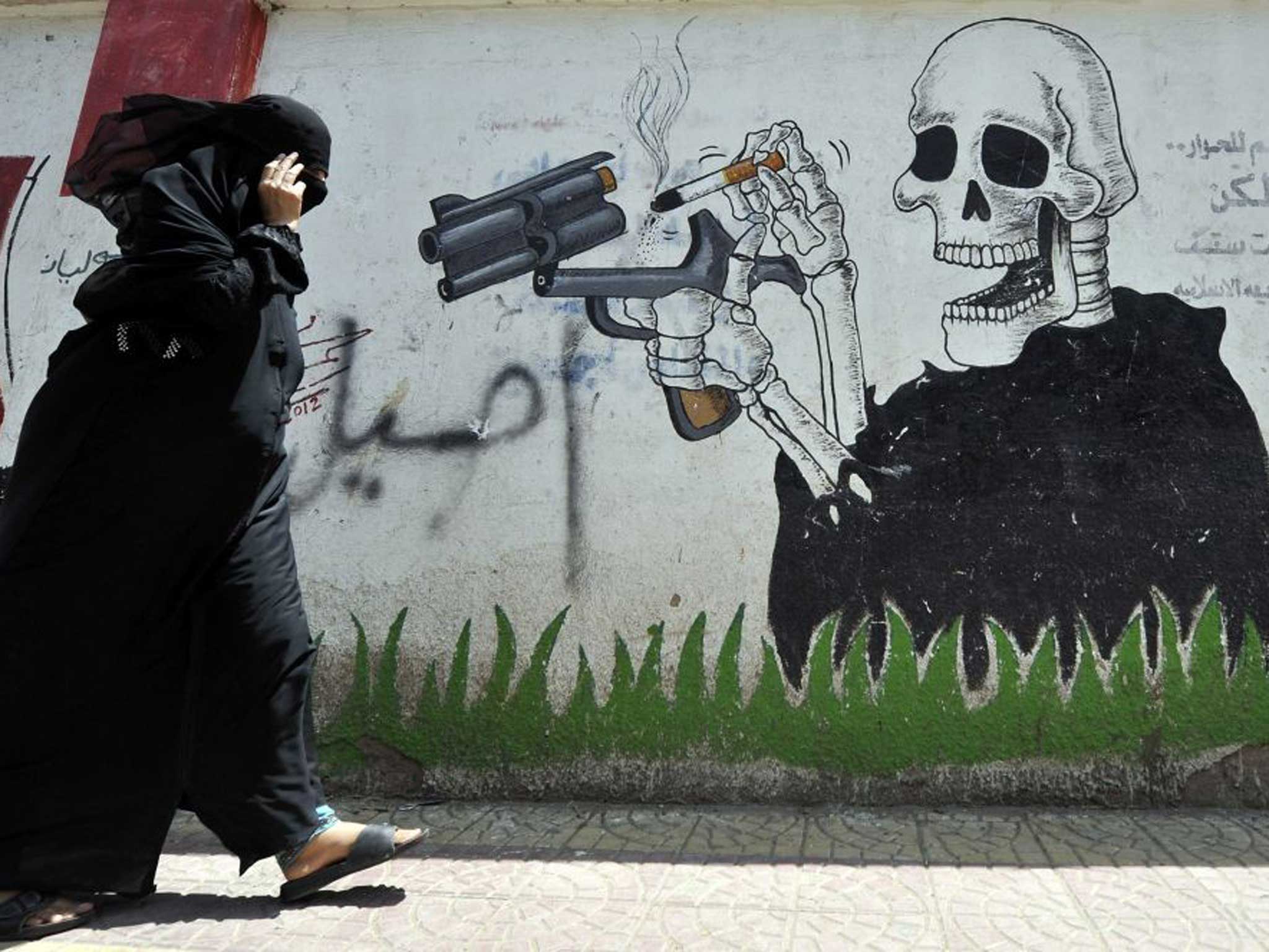 A Yemeni woman walks past an anti-smoking drawing