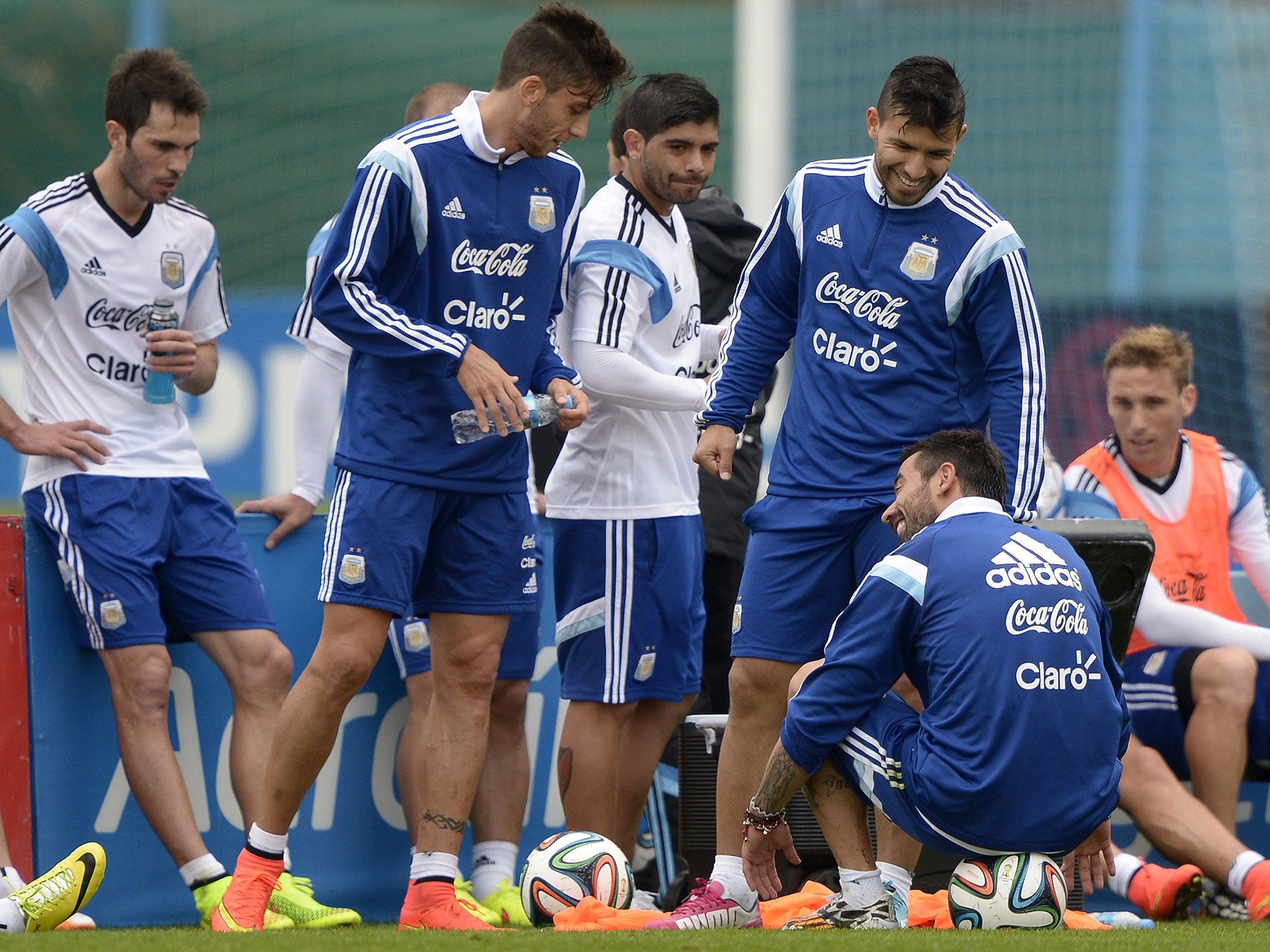 Argentina's forward Ezequiel Lavezzi seats on a ball as forward Sergio Aguero (R) smiles next to teammates midfielder Ever Banega (C) and midfielder Ricky Alvarez during a training session