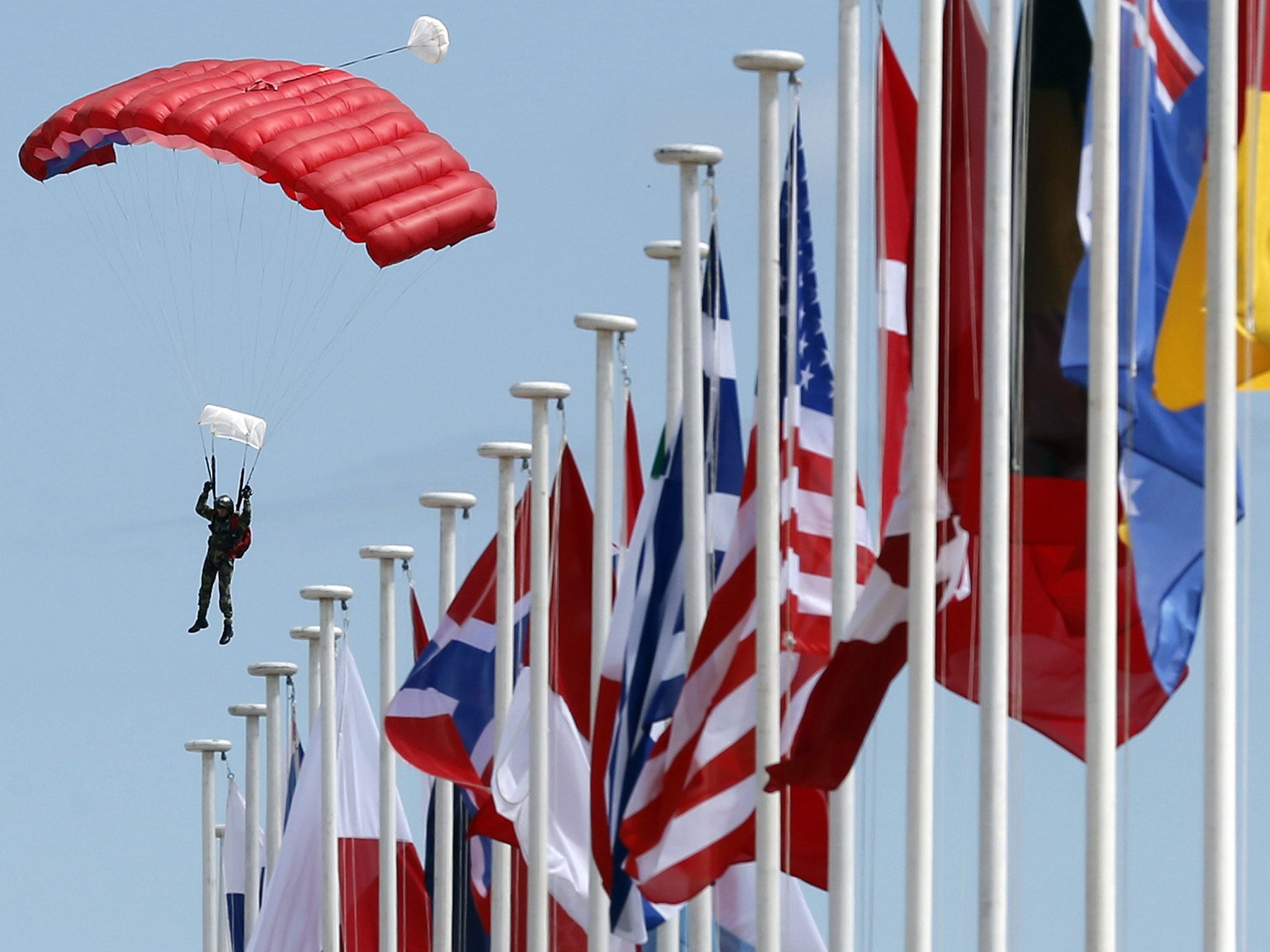 A paratrooper lands on Sword Beach near international flags during a D-Day celebration rehearsal in Ouistreham, on the Normandy coast