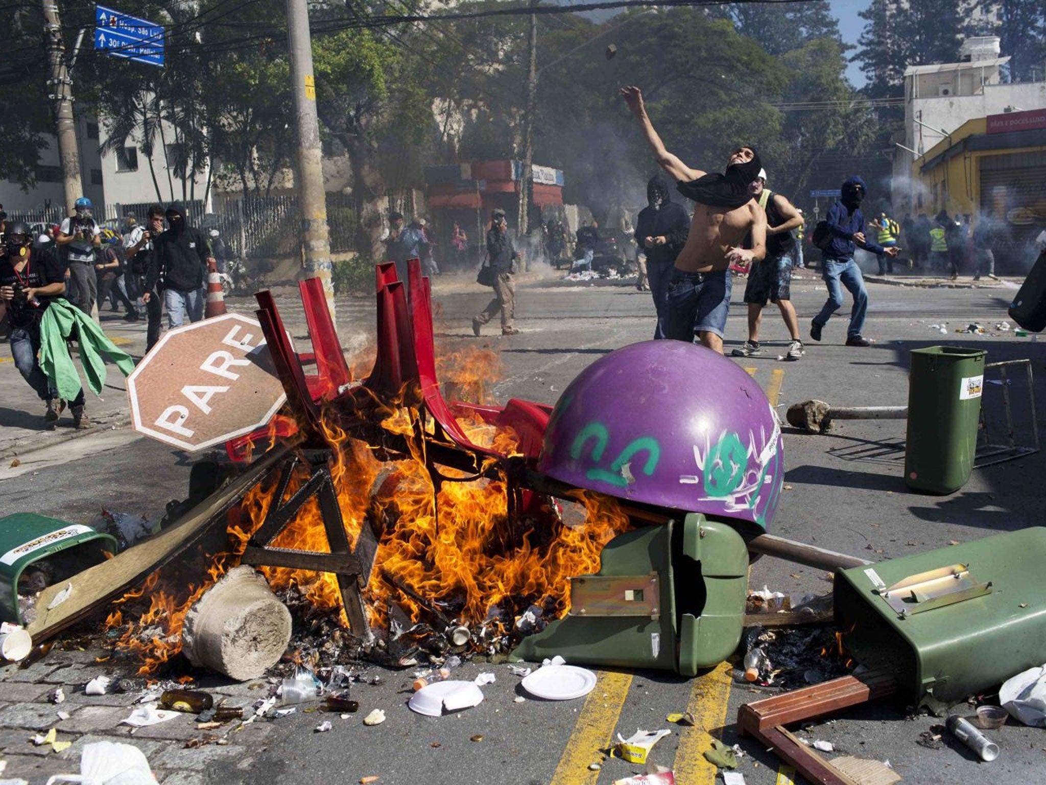 A masked man throws a stone towards riot policemen during a protest by people demanding better public services and against the money spent on the World Cup soccer tournament in Sao Paulo